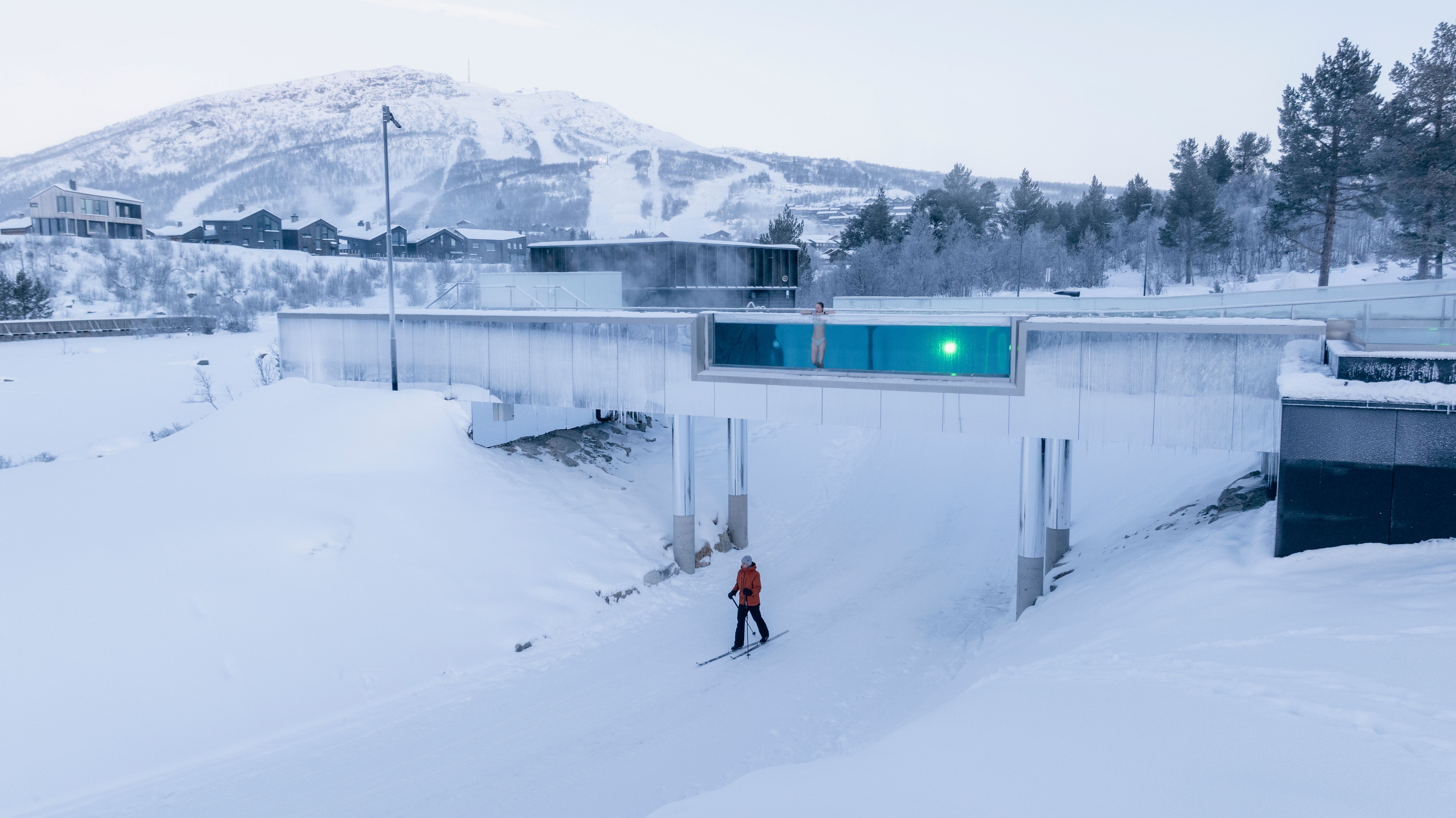 A person cross-country skiing beneath another swimming in the outdoor infinity pool at Hovden Fjellbad Spa
