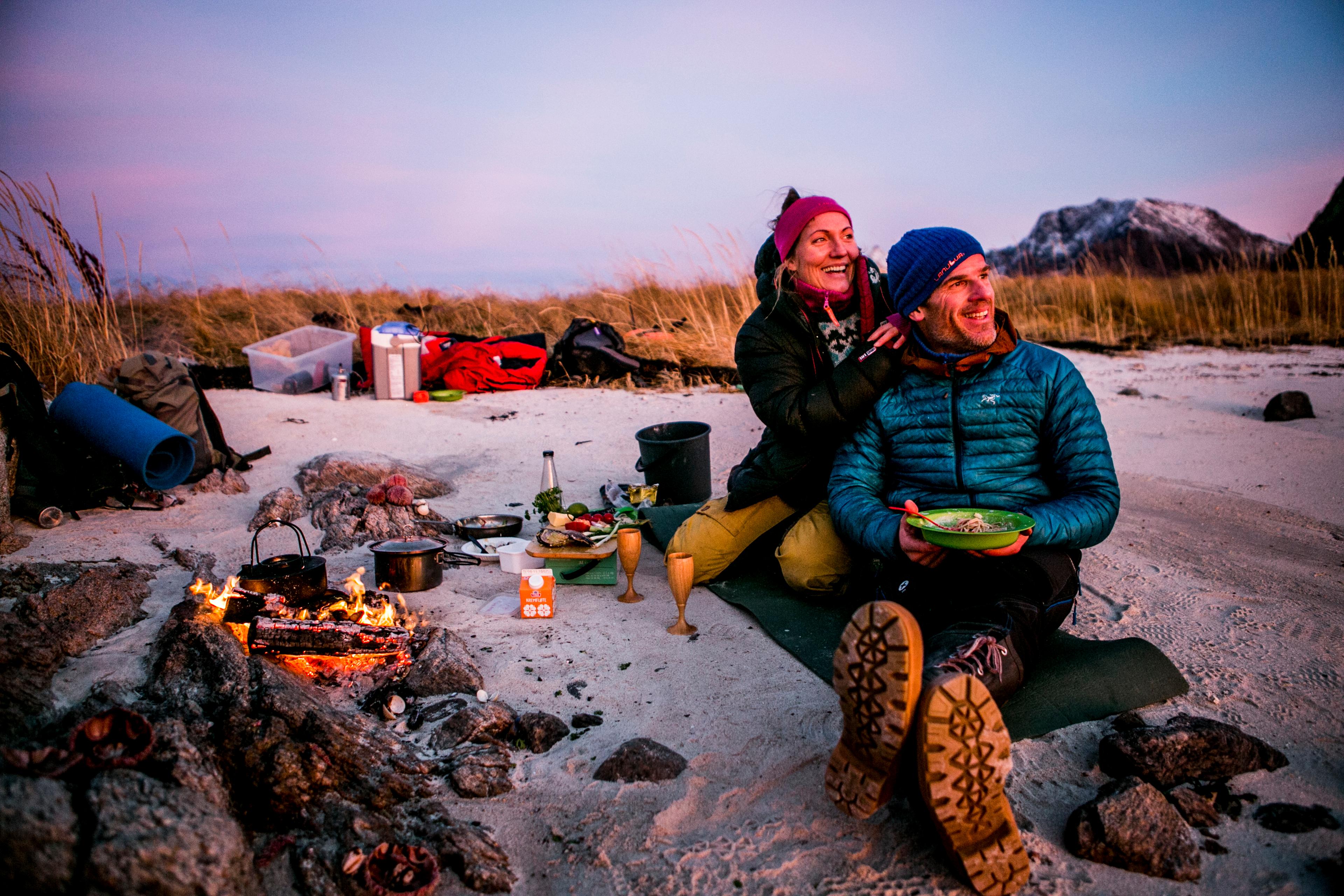 Two campers having a cosy campfire dinner on a beach in the evening light
