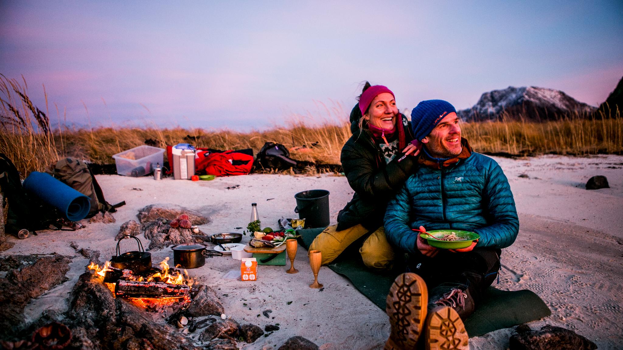 Två campare som har en mysig grillmiddag på stranden i kvällssol