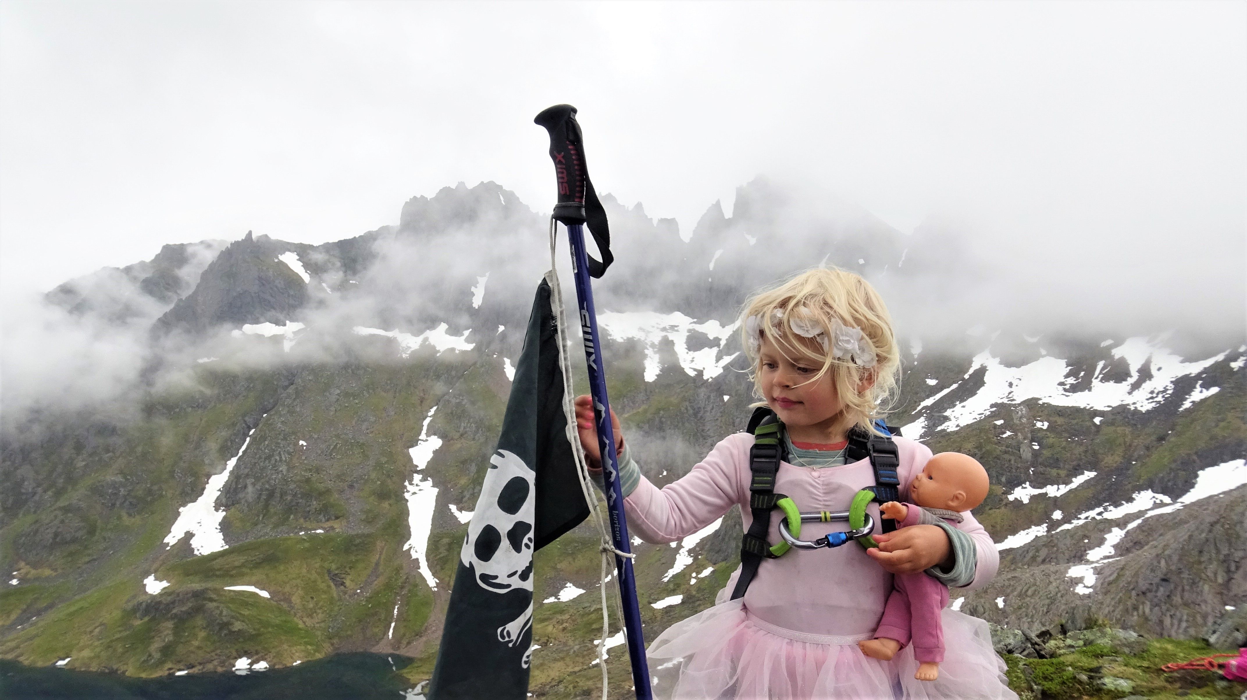 A young girl wearing a ballerina skirt and holding a pirate flag at the top of Grønetinden mountain in Molladalen, Fjord Norway