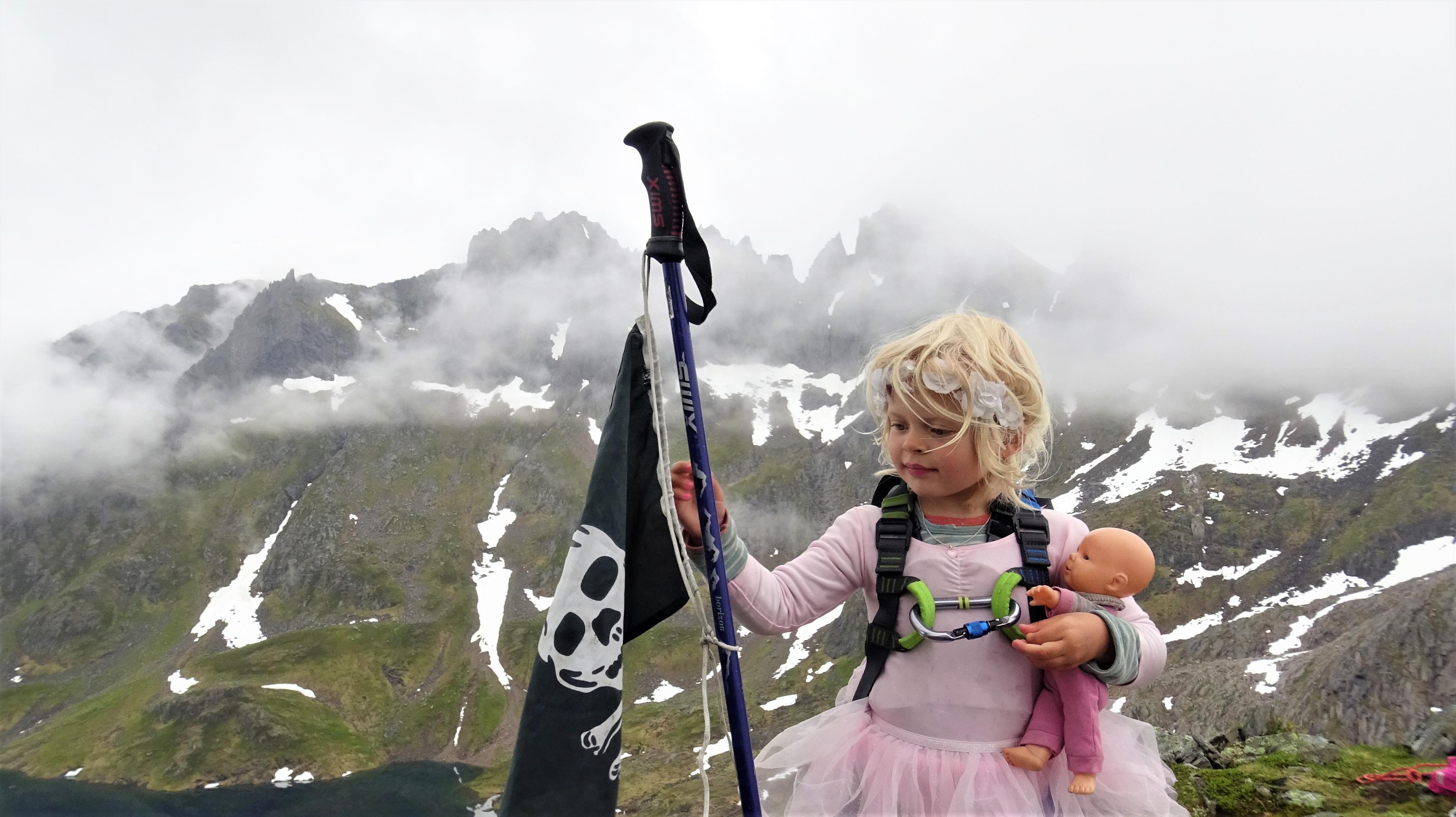 A young girl wearing a ballerina skirt and holding a pirate flag at the top of Grønetinden mountain in Molladalen, Fjord Norway