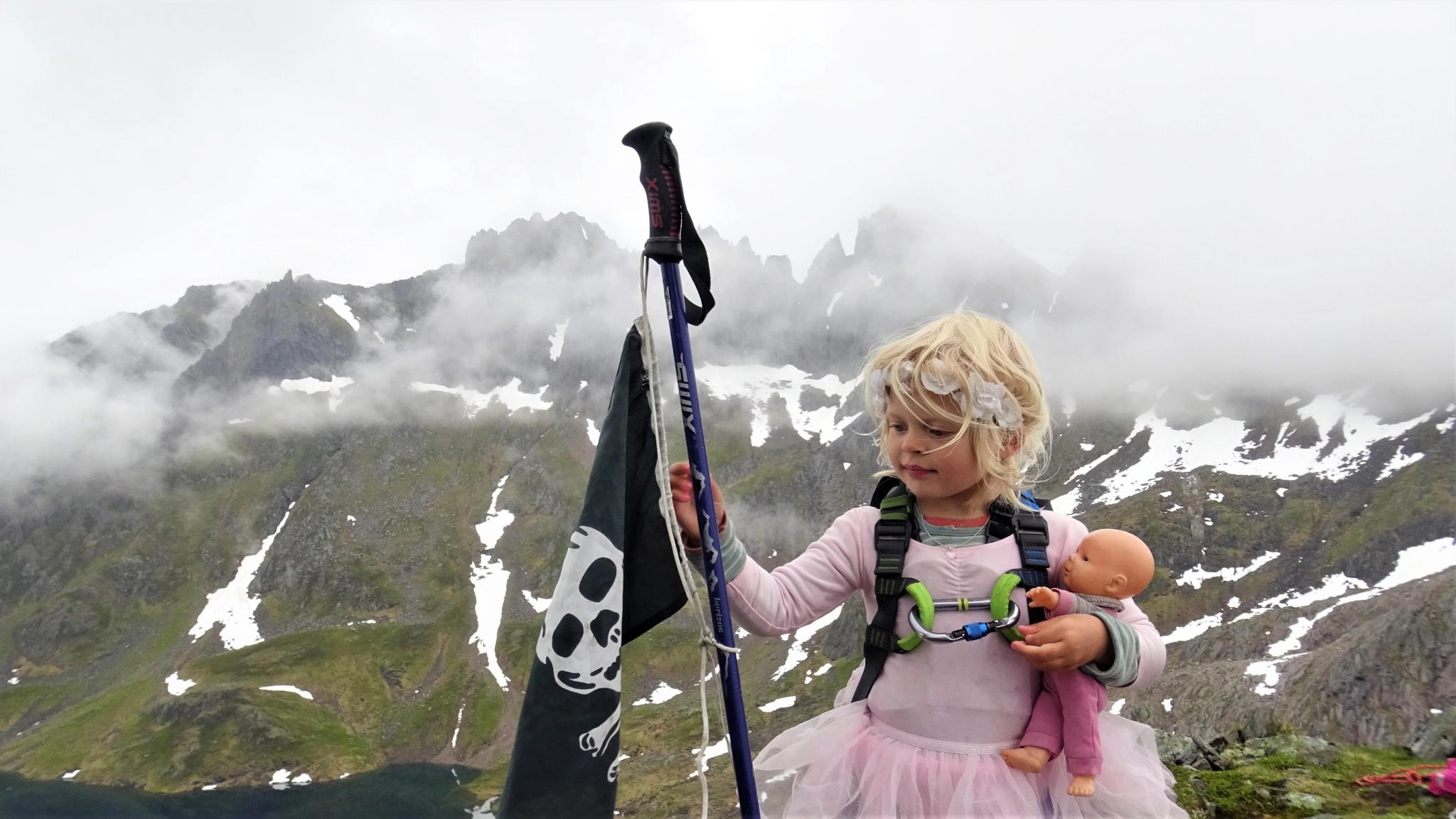 A young girl wearing a ballerina skirt and holding a pirate flag at the top of Grønetinden mountain in Molladalen, Fjord Norway