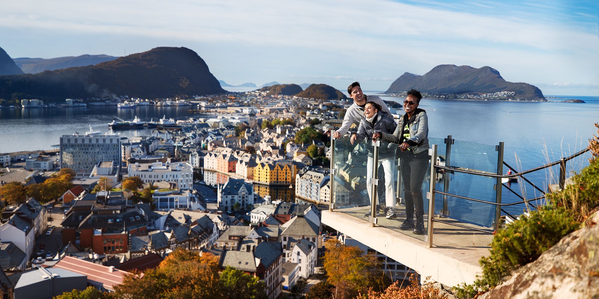 Tres personas disfrutan de las vistas desde un mirador en lo alto del monte Aksla, en Ålesund, la Noruega de los fiordos, en un día soleado.