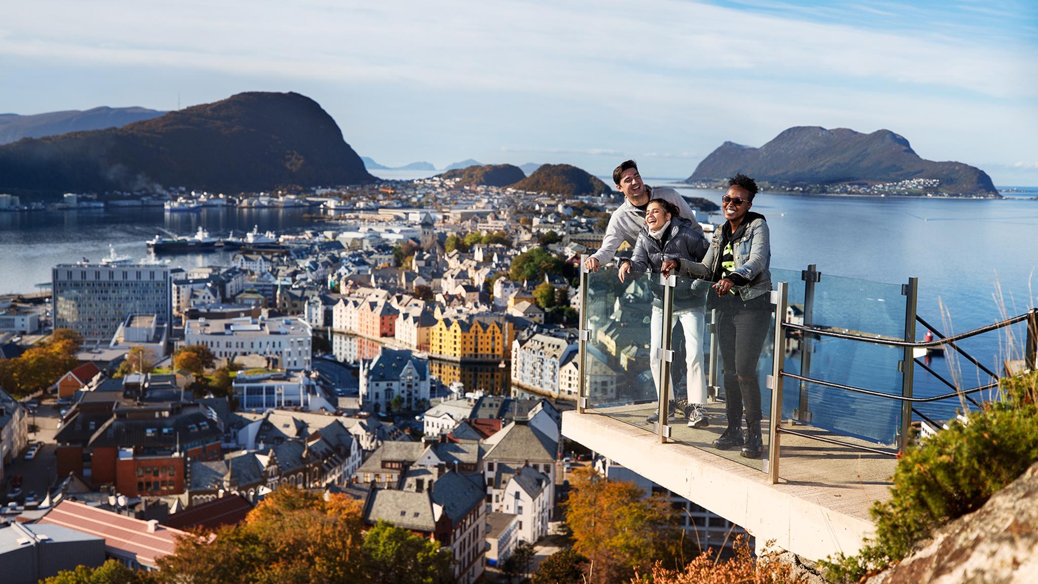 Three people standing on a viewing platform at Mount Aksla in Ålesund, Fjord Norway