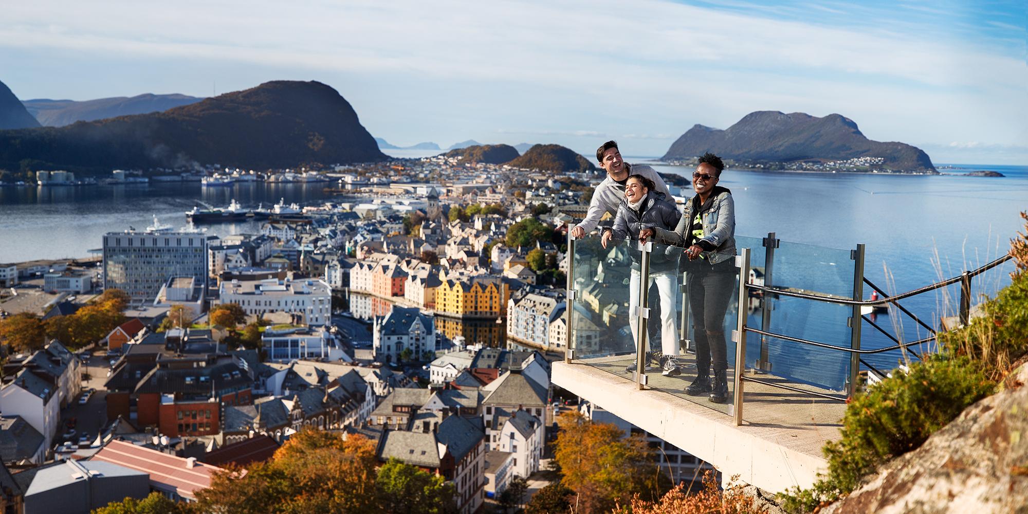 Tres personas disfrutan de las vistas desde un mirador en lo alto del monte Aksla, en Ålesund, la Noruega de los fiordos, en un día soleado.