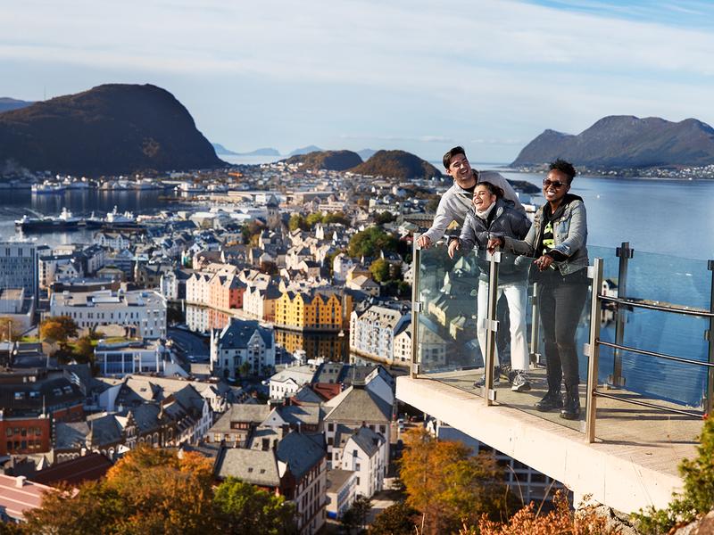 Tres personas disfrutan de las vistas desde un mirador en lo alto del monte Aksla, en Ålesund, la Noruega de los fiordos, en un día soleado.