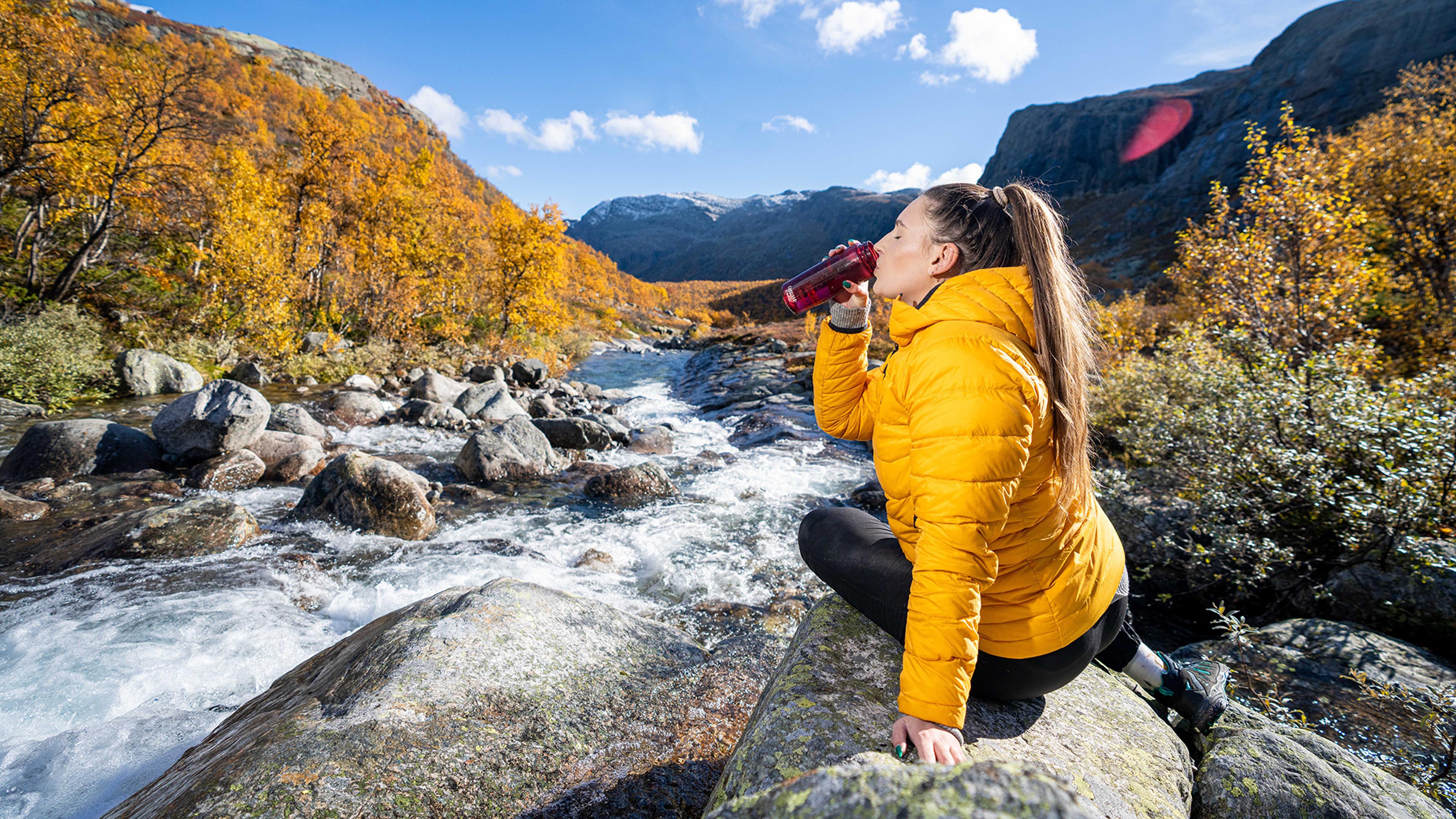 Woman drinking water from a river, Hemsedal, Norway.