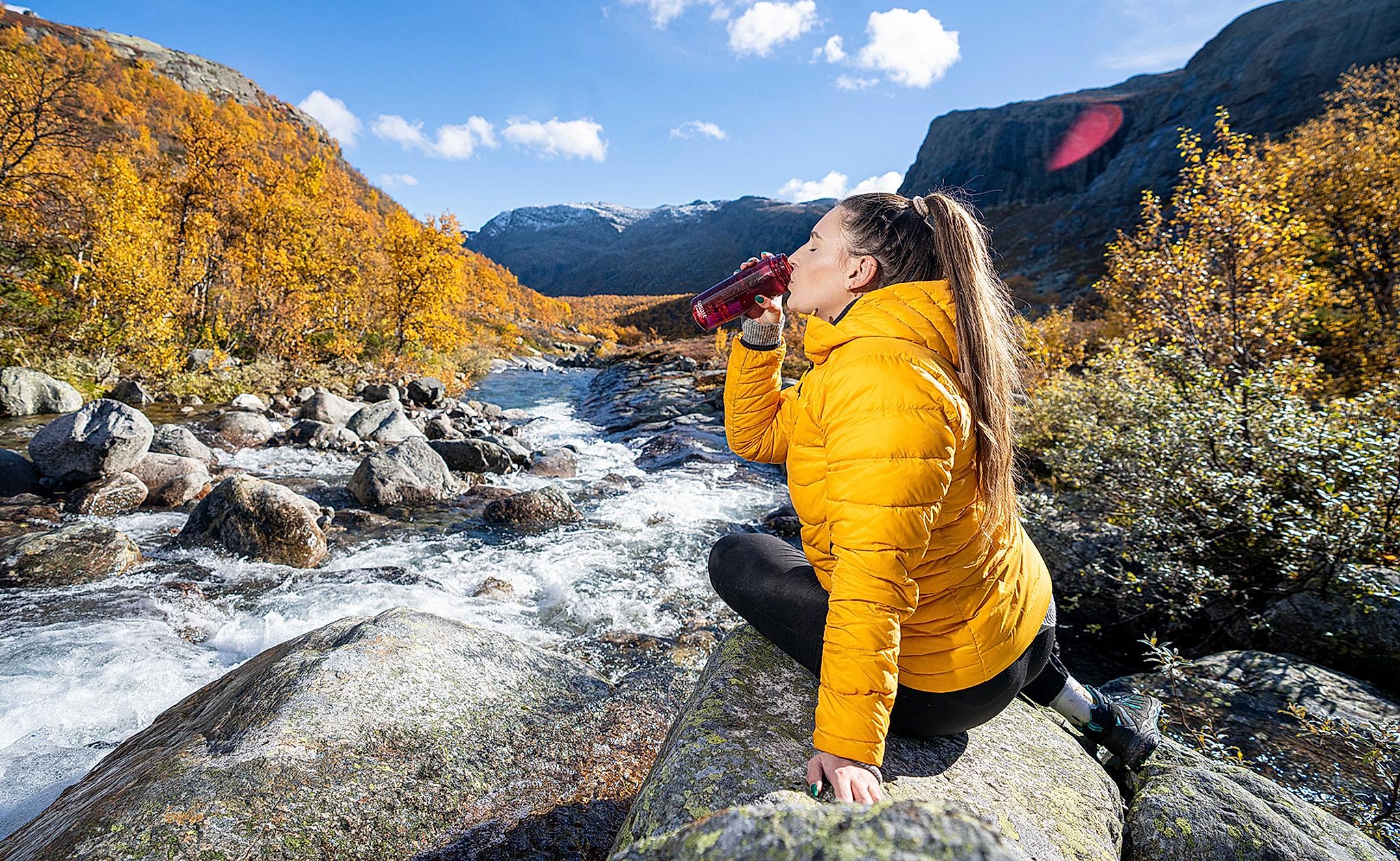 Woman drinking water from a river, Hemsedal, Norway.