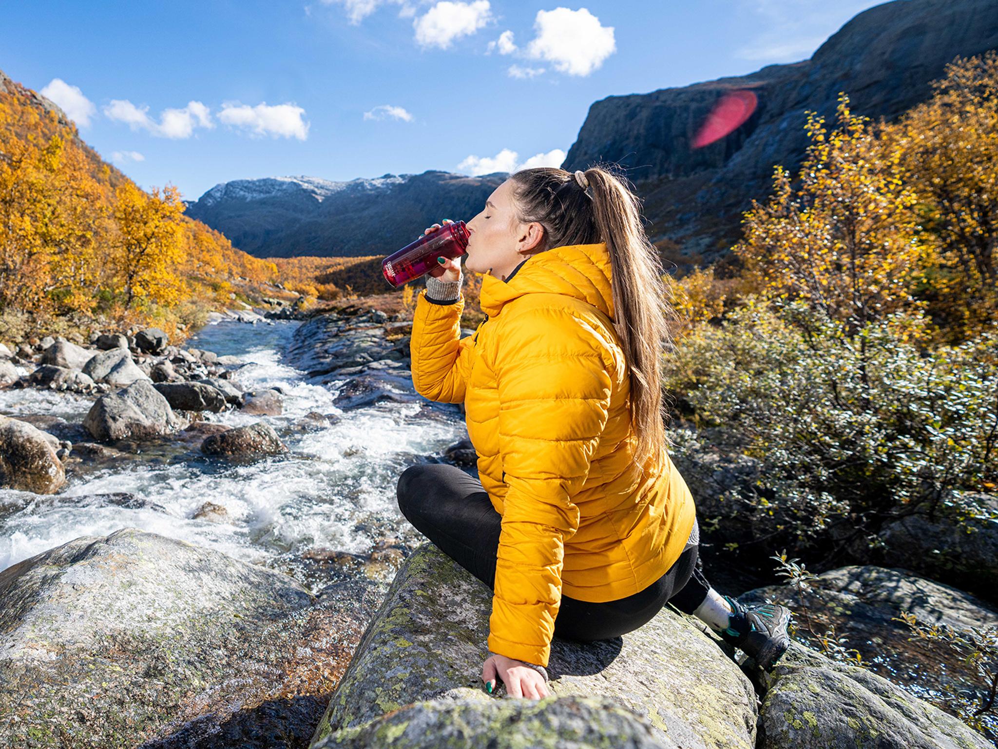 Woman drinking water from a river, Hemsedal, Norway.