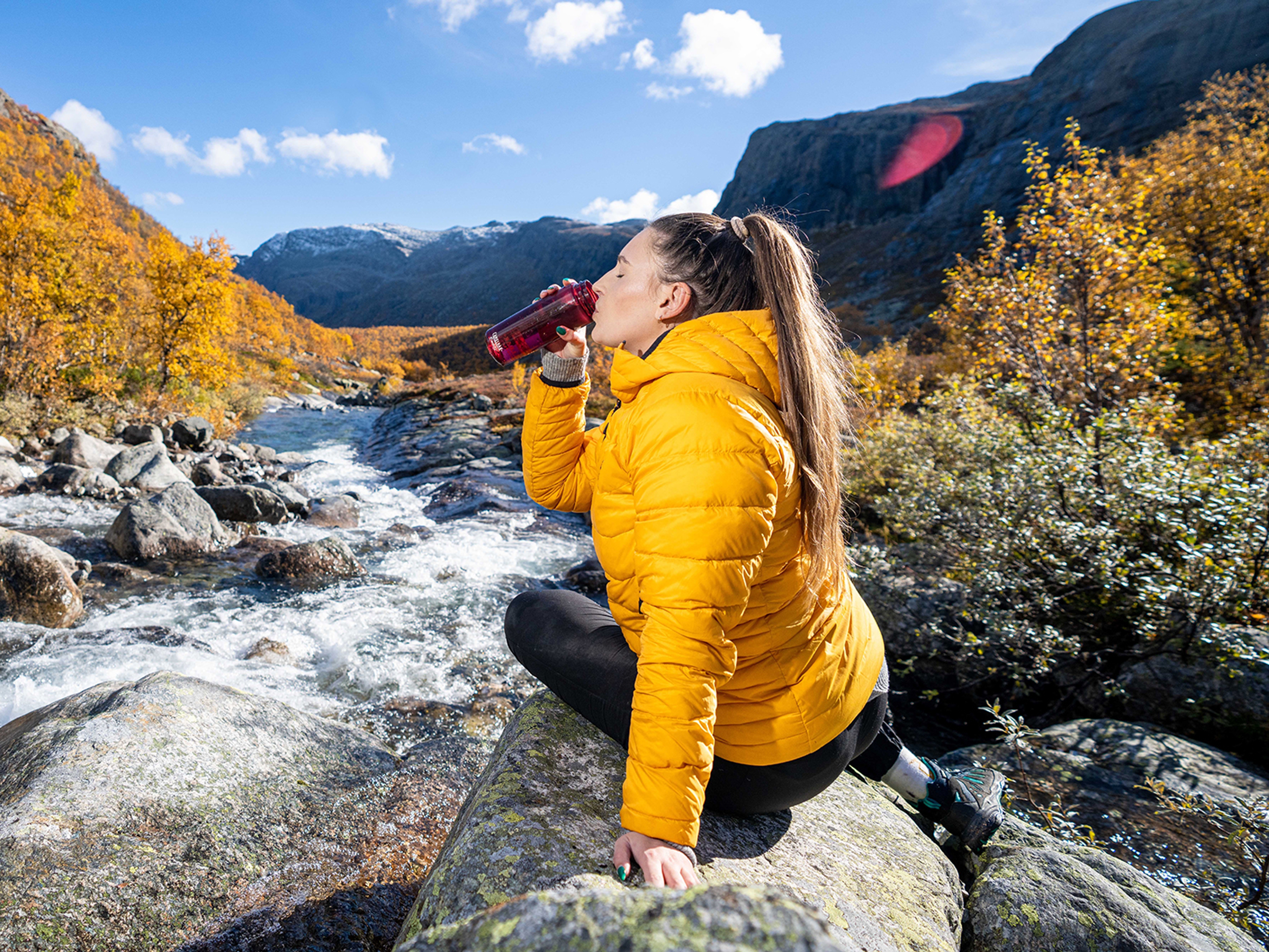 Woman drinking water from a river, Hemsedal, Norway.