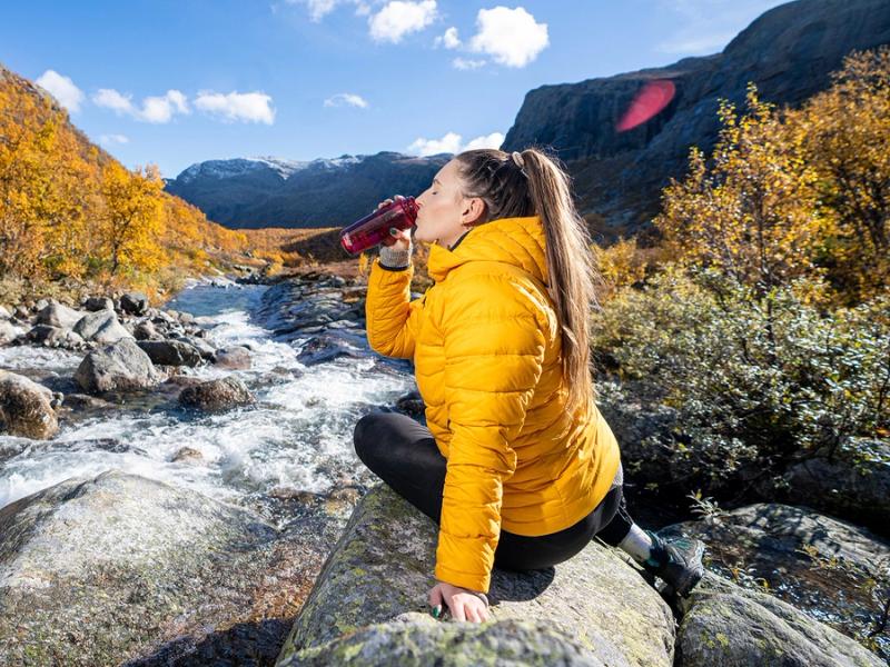 Woman drinking water from a river, Hemsedal, Norway.