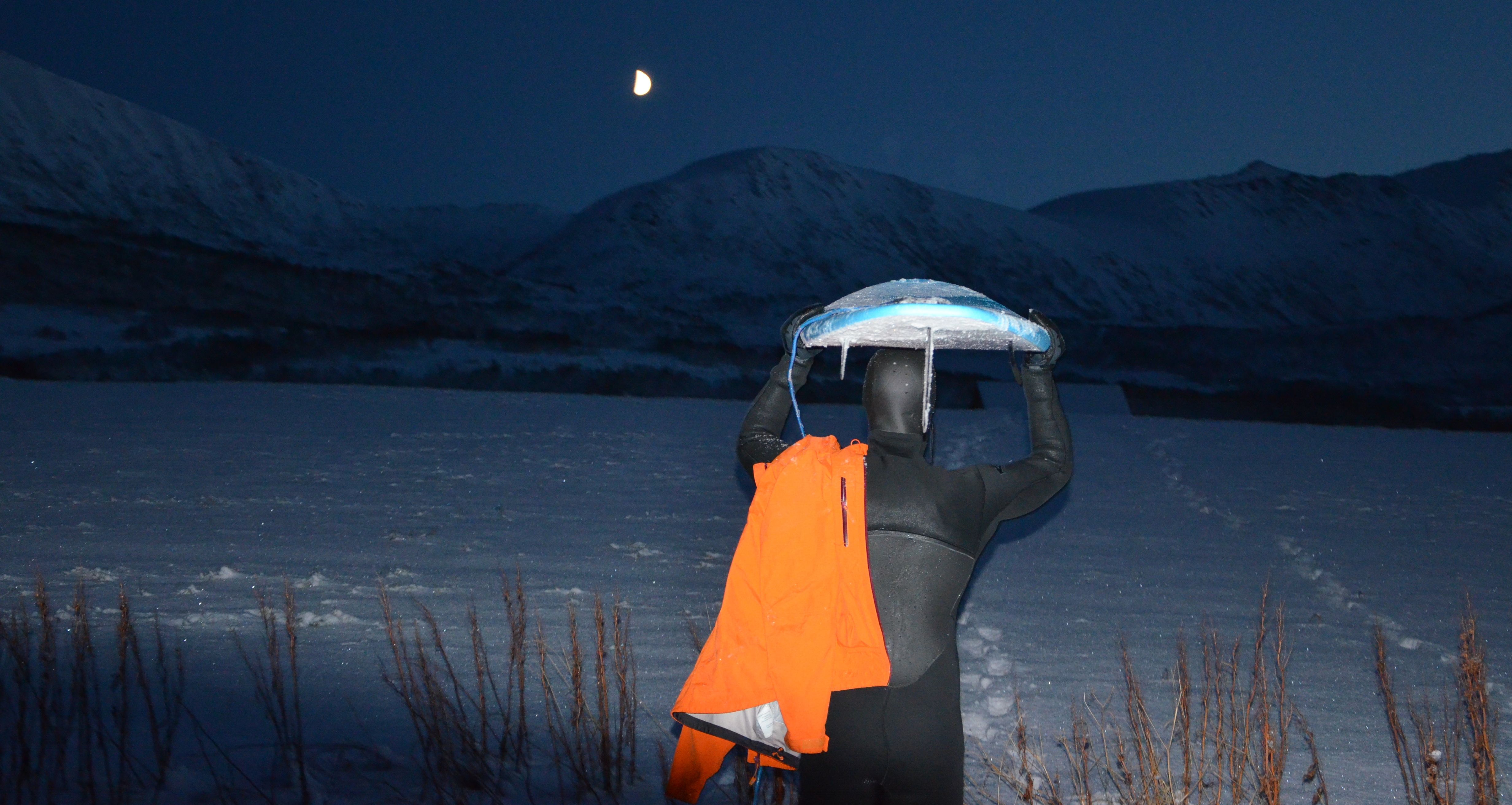 Anders Stave at night holding a surf board over his head in Andøya in Northern Norway