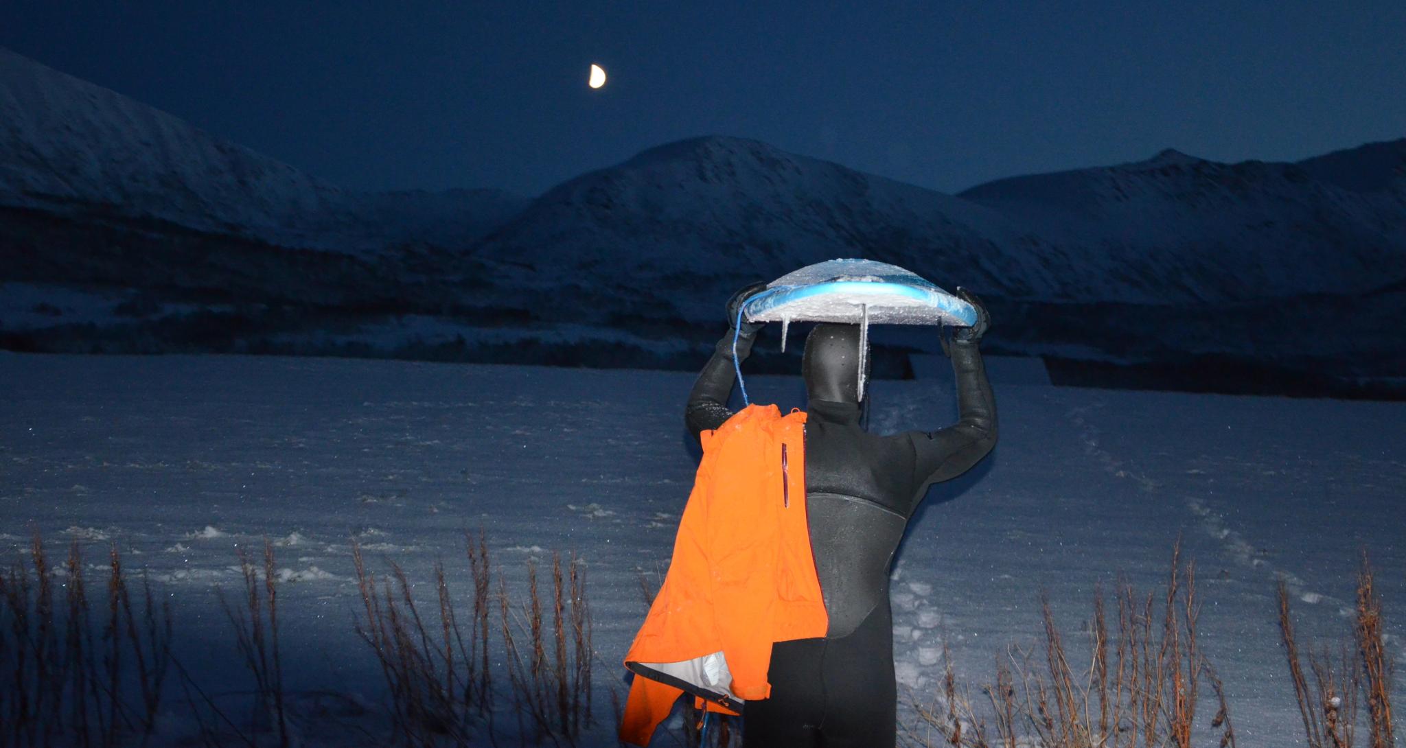 Anders Stave at night holding a surf board over his head in Andøya in Northern Norway