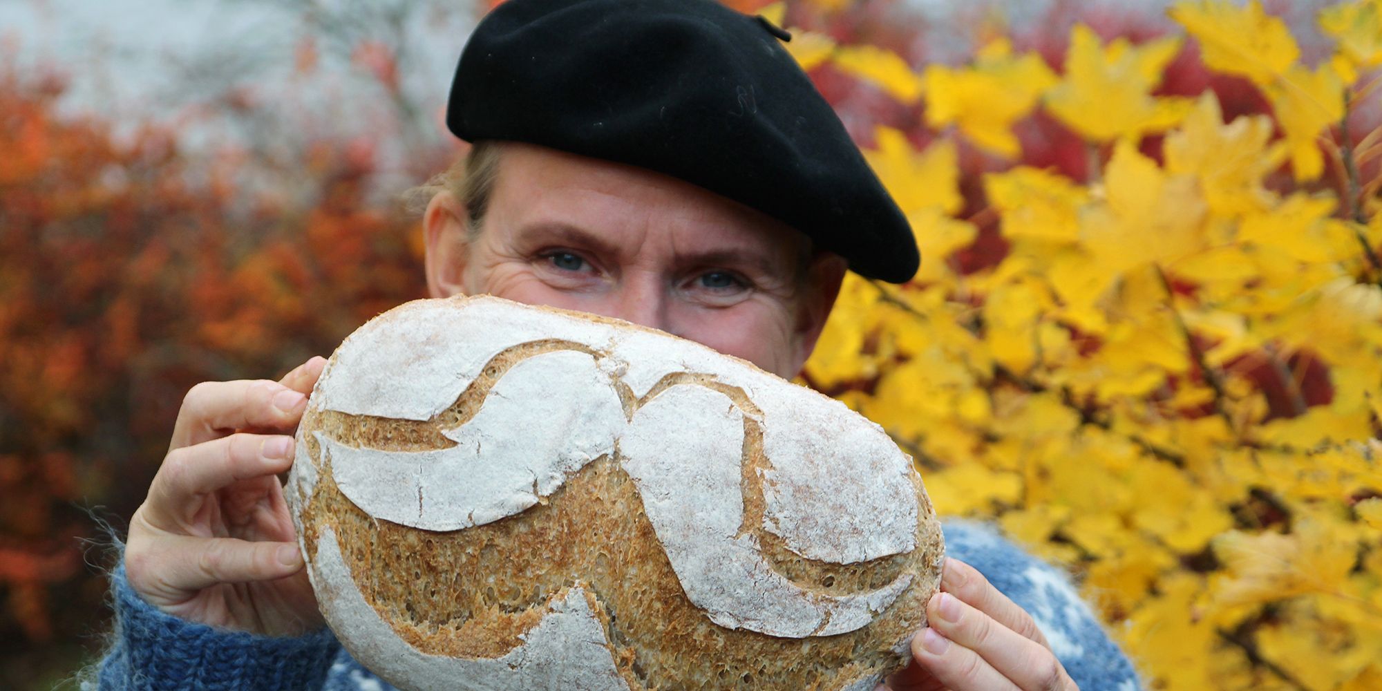 A man is holding up a bread with flour designed as a moustache in Norway