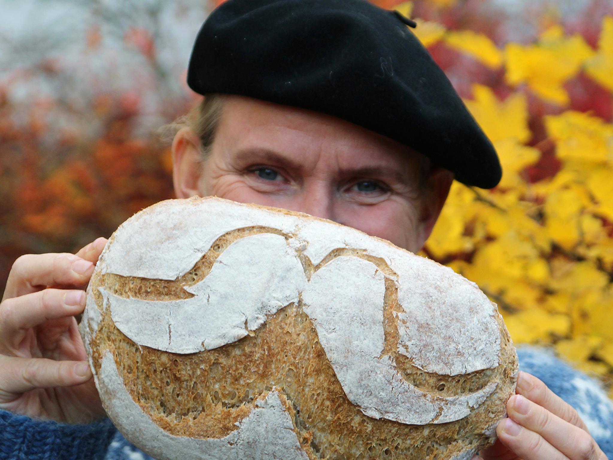 A man is holding up a bread with flour designed as a moustache in Norway