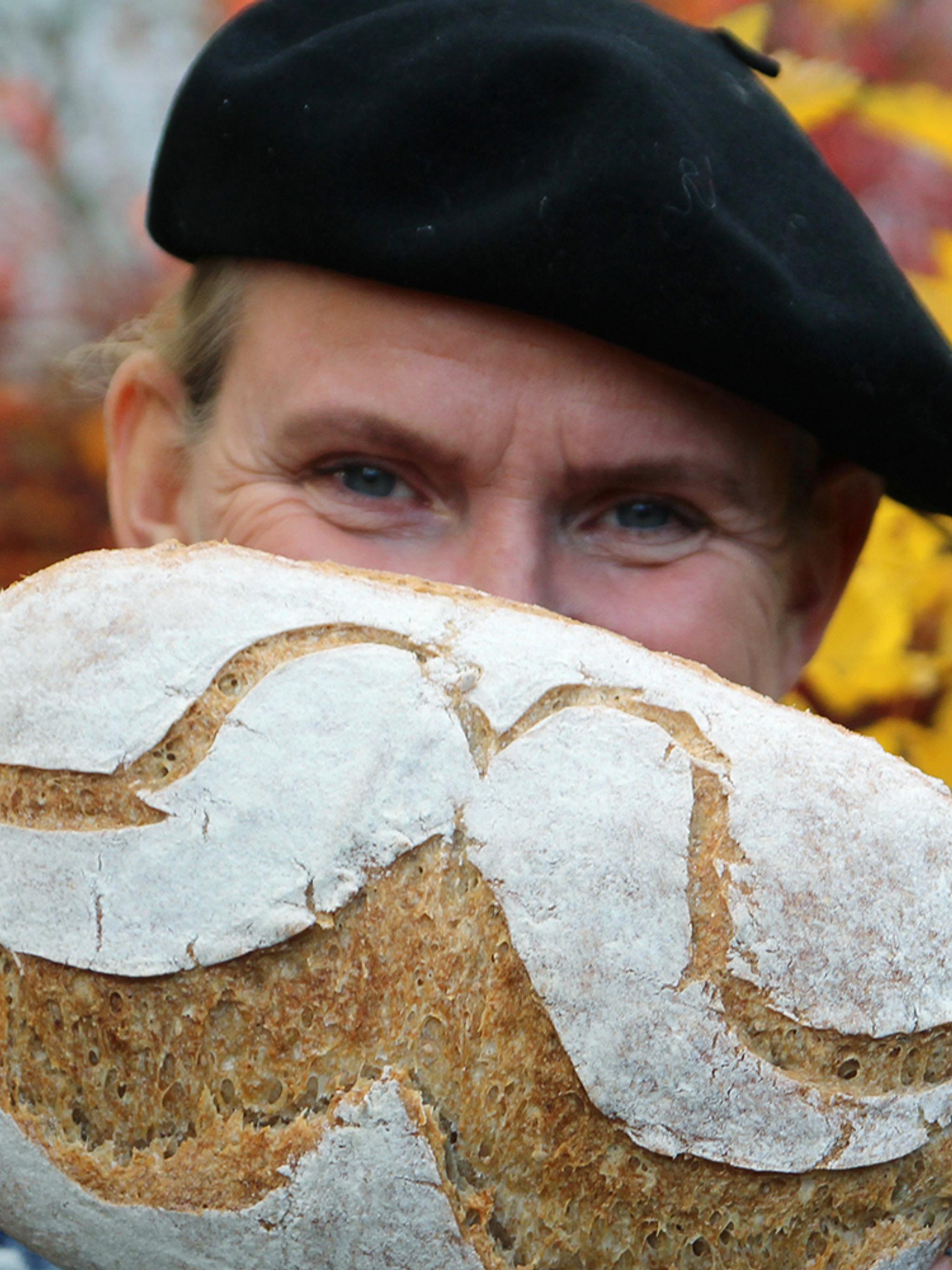 A man is holding up a bread with flour designed as a moustache in Norway