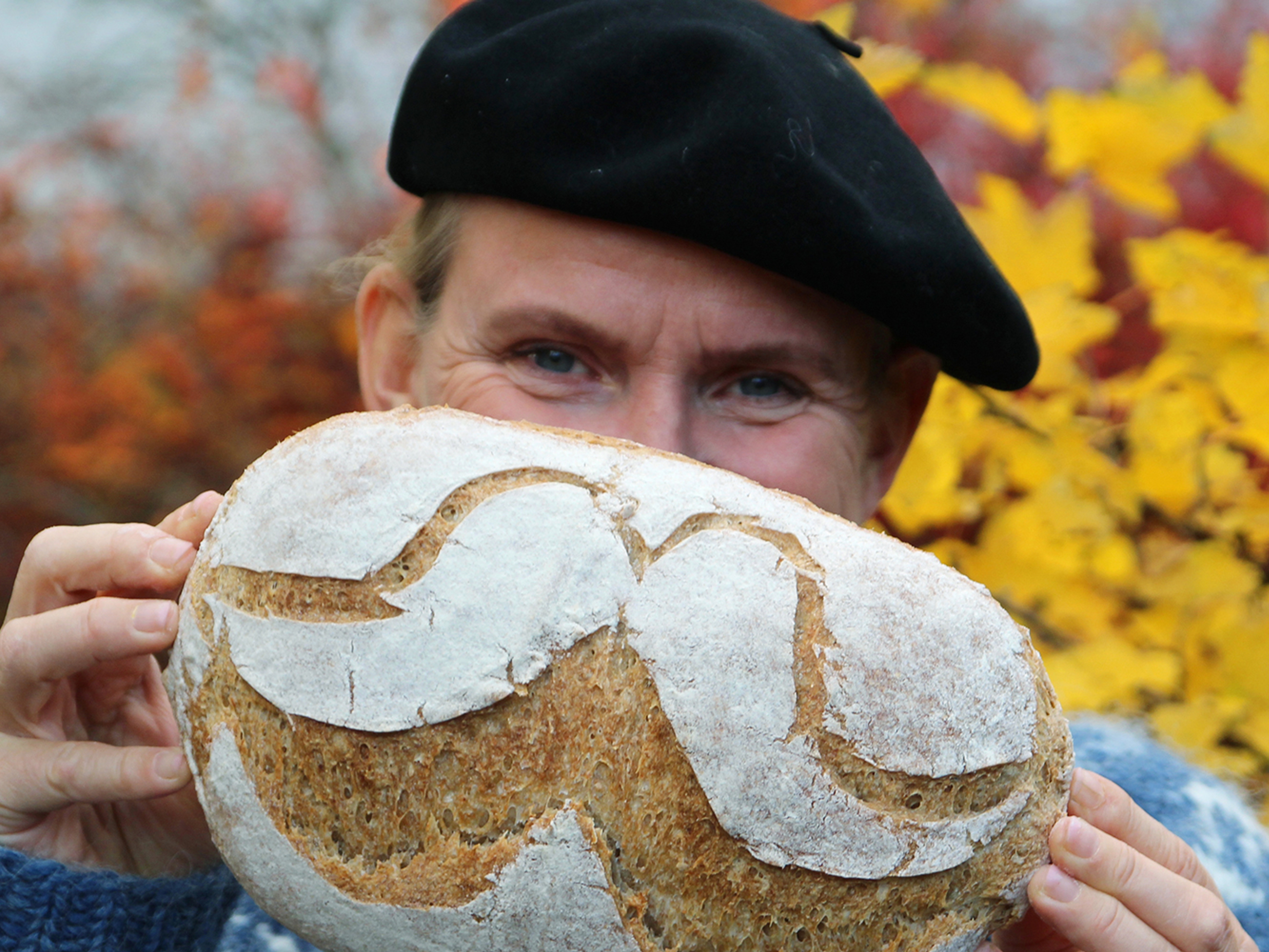 A man is holding up a bread with flour designed as a moustache in Norway