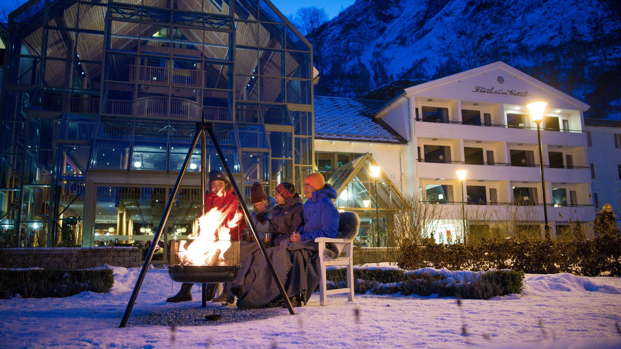 People sitting around the bonfire outside Fretheim Hotel in winter