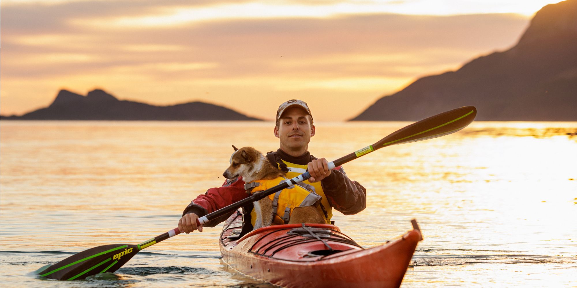 A man and a dog is kayaking in the midnight sun in Northern Norway.