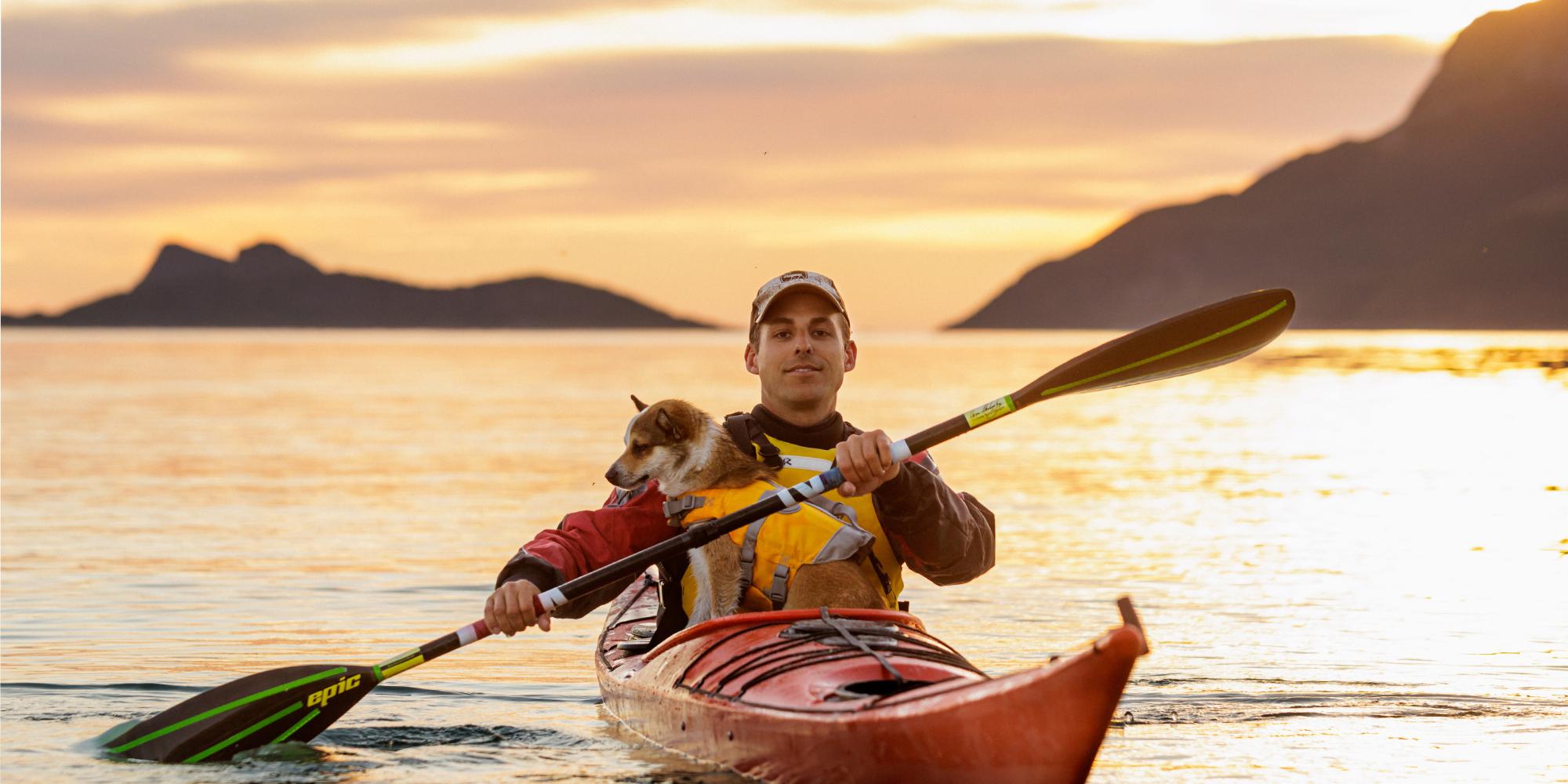A man and a dog is kayaking in the midnight sun in Northern Norway.
