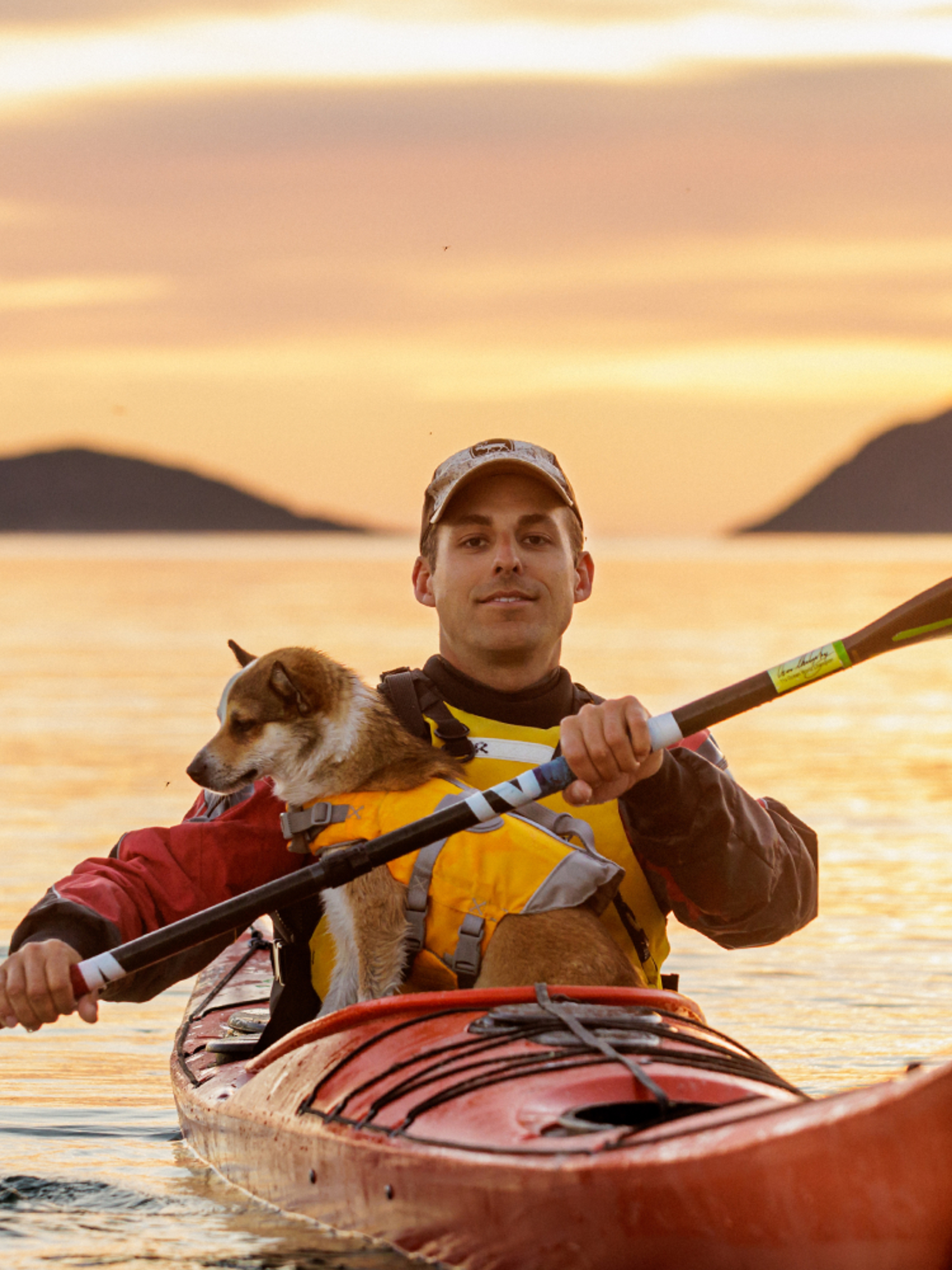 En mann og en hund kjører kajakk i midnattssolen i Nord-Norge.