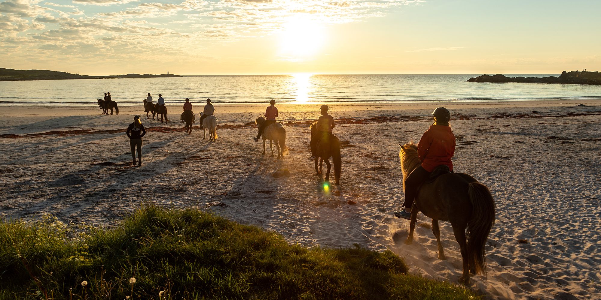 People horseback riding at a beach at sunset in Lofoten, Northern Norway