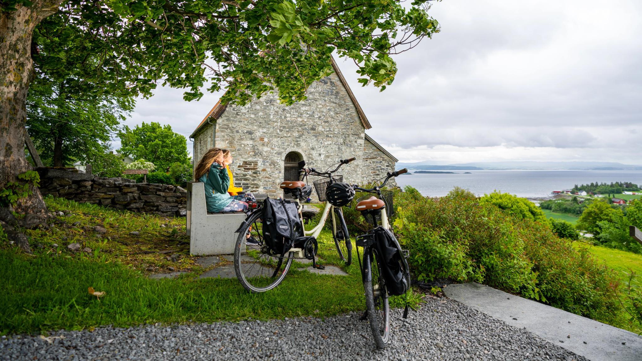 Two woman sitting on a bench outside the medieval granit church Sakshaug old church, The Golden Road, Inderøy