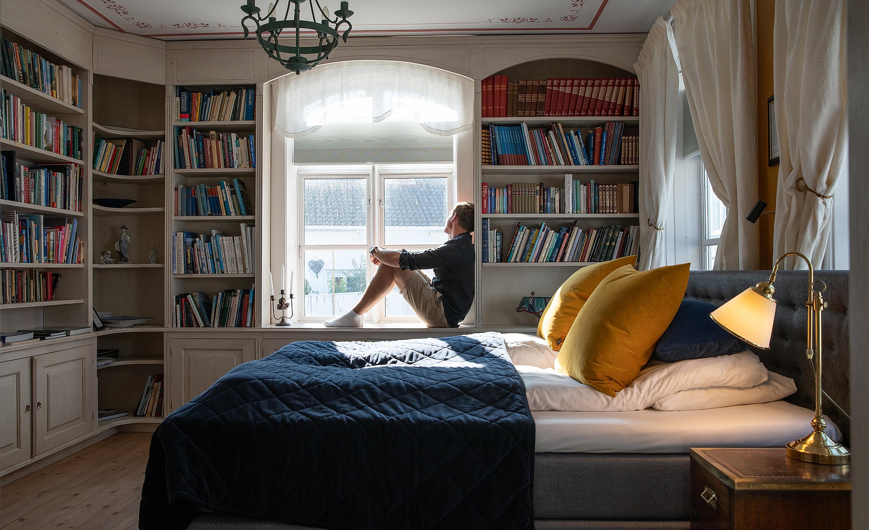 En person sidder på en seng på Det Lille Hotel i Risør, Norge