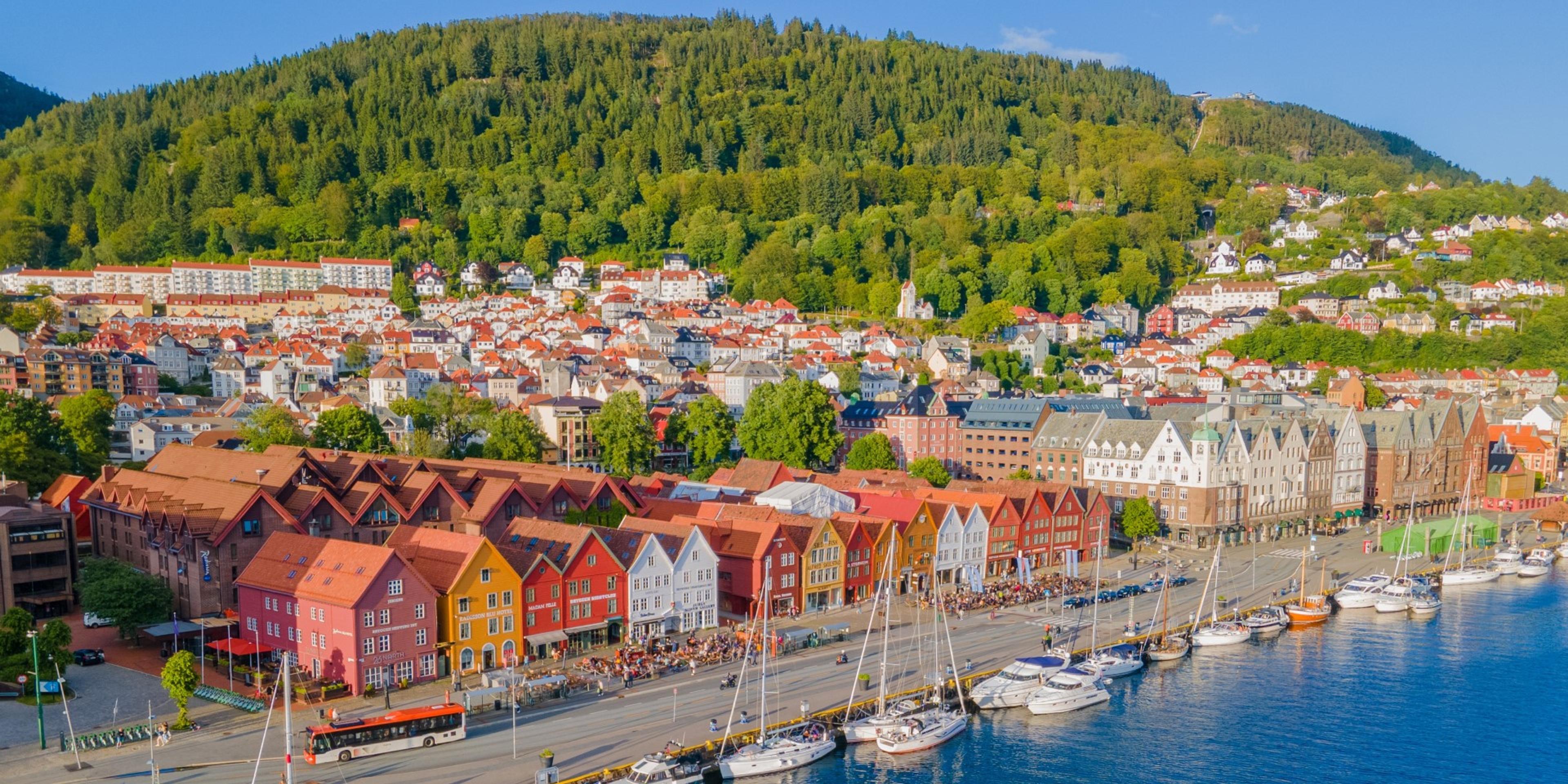 Harbor with red waterfront buildings and boats, backed by forested hillsid