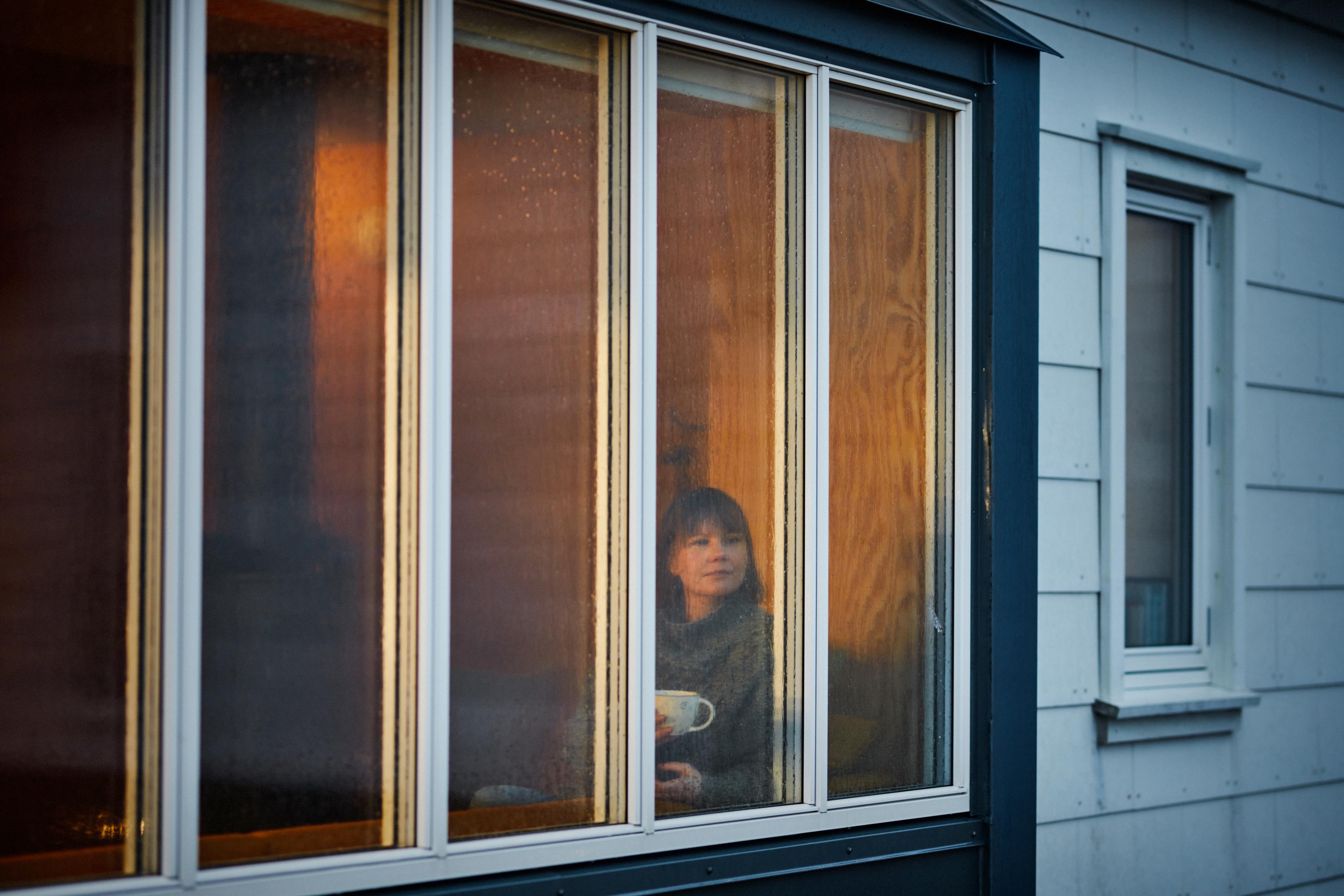 Woman with a coffee cup looking at the rain from behind the window