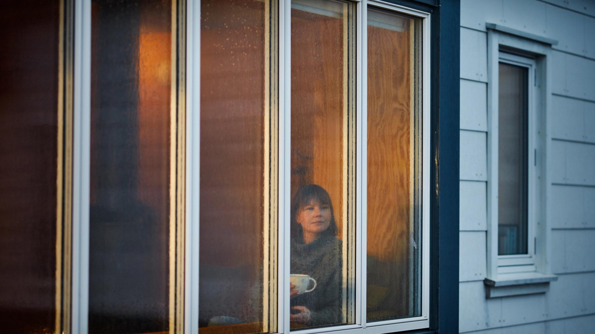 Woman with a coffee cup looking at the rain from behind the window