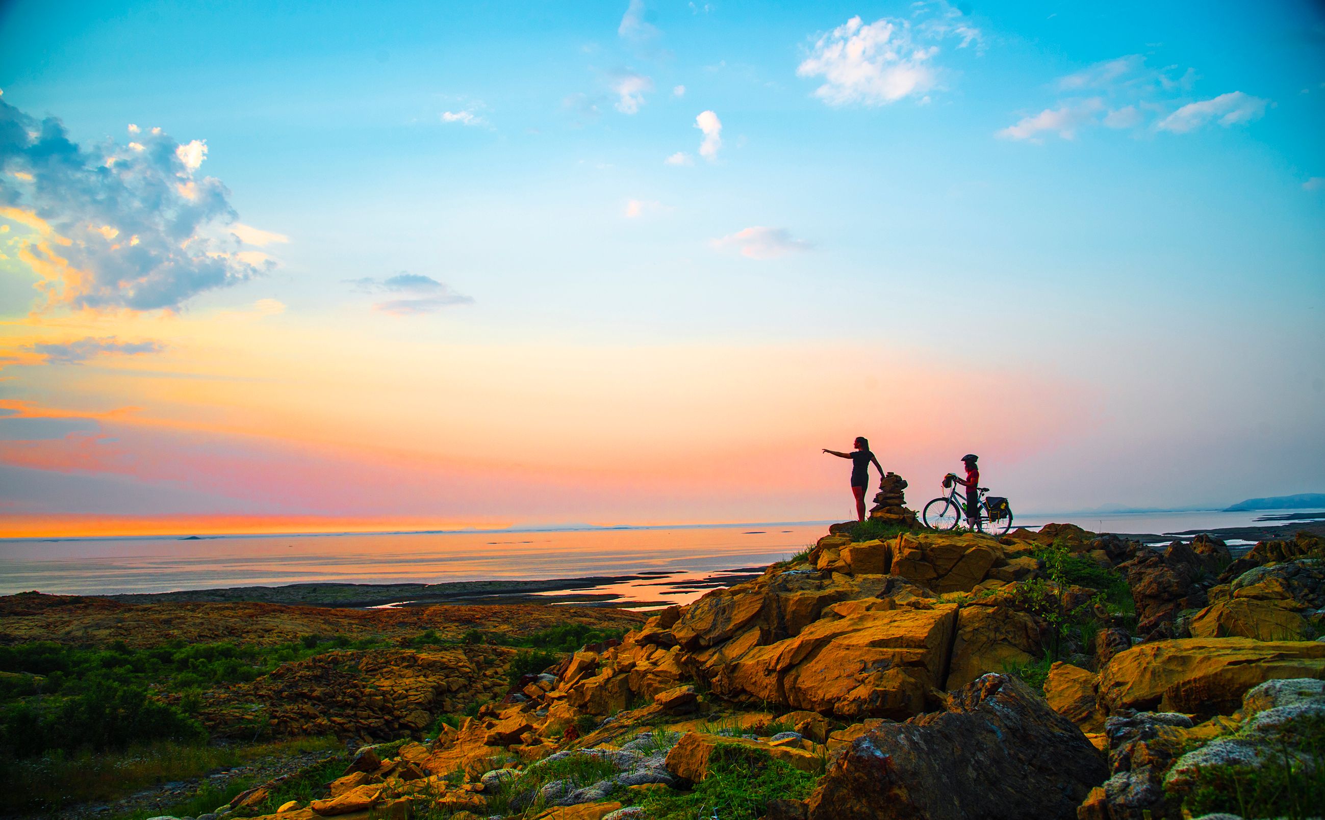 A hiker and a cyclist standing side by side watching the sunset at the Leka island in Trøndelag.