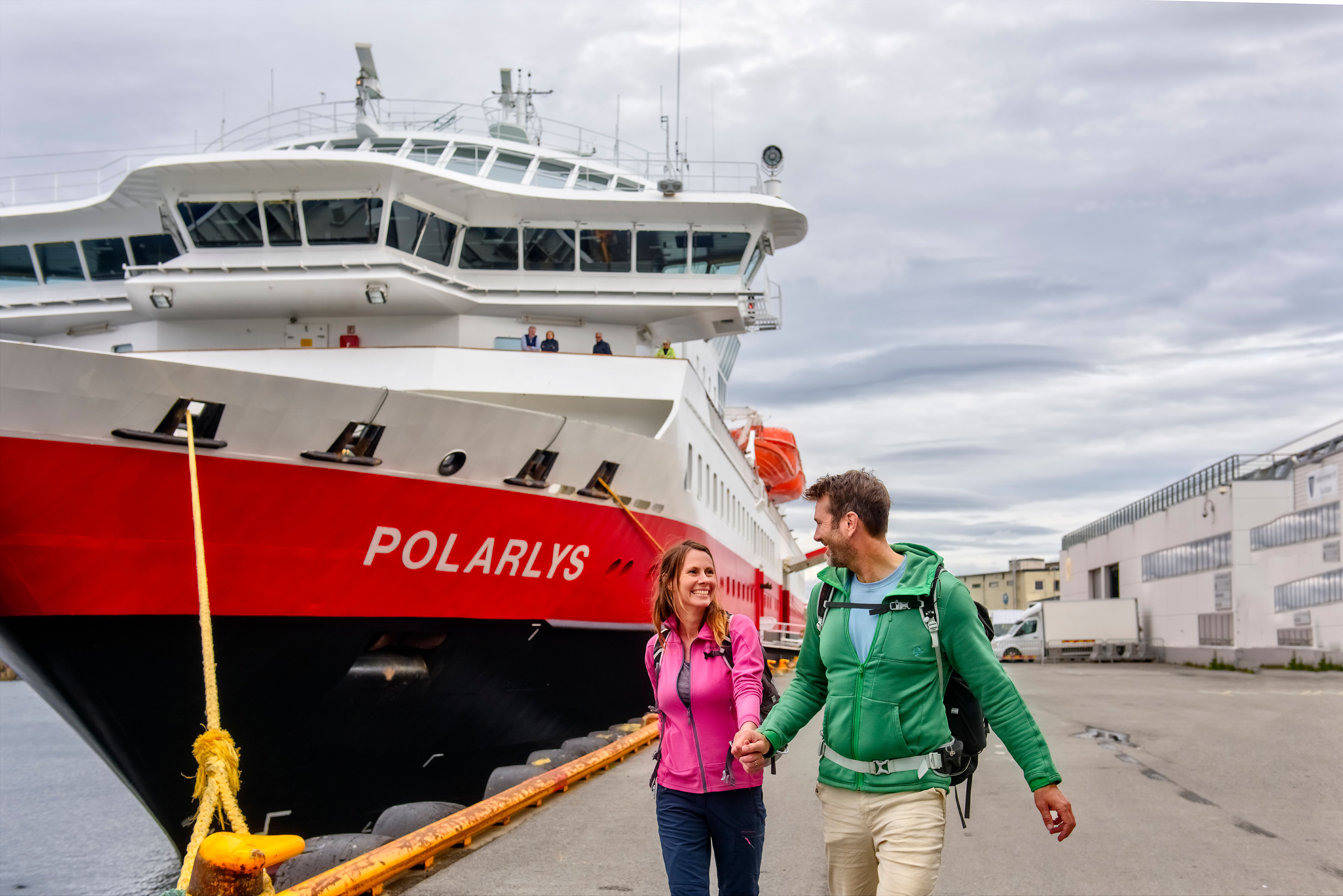 A smiling couple in front of the MS Polarlys Hurtigruten ship in Lofoten, Northern Norway