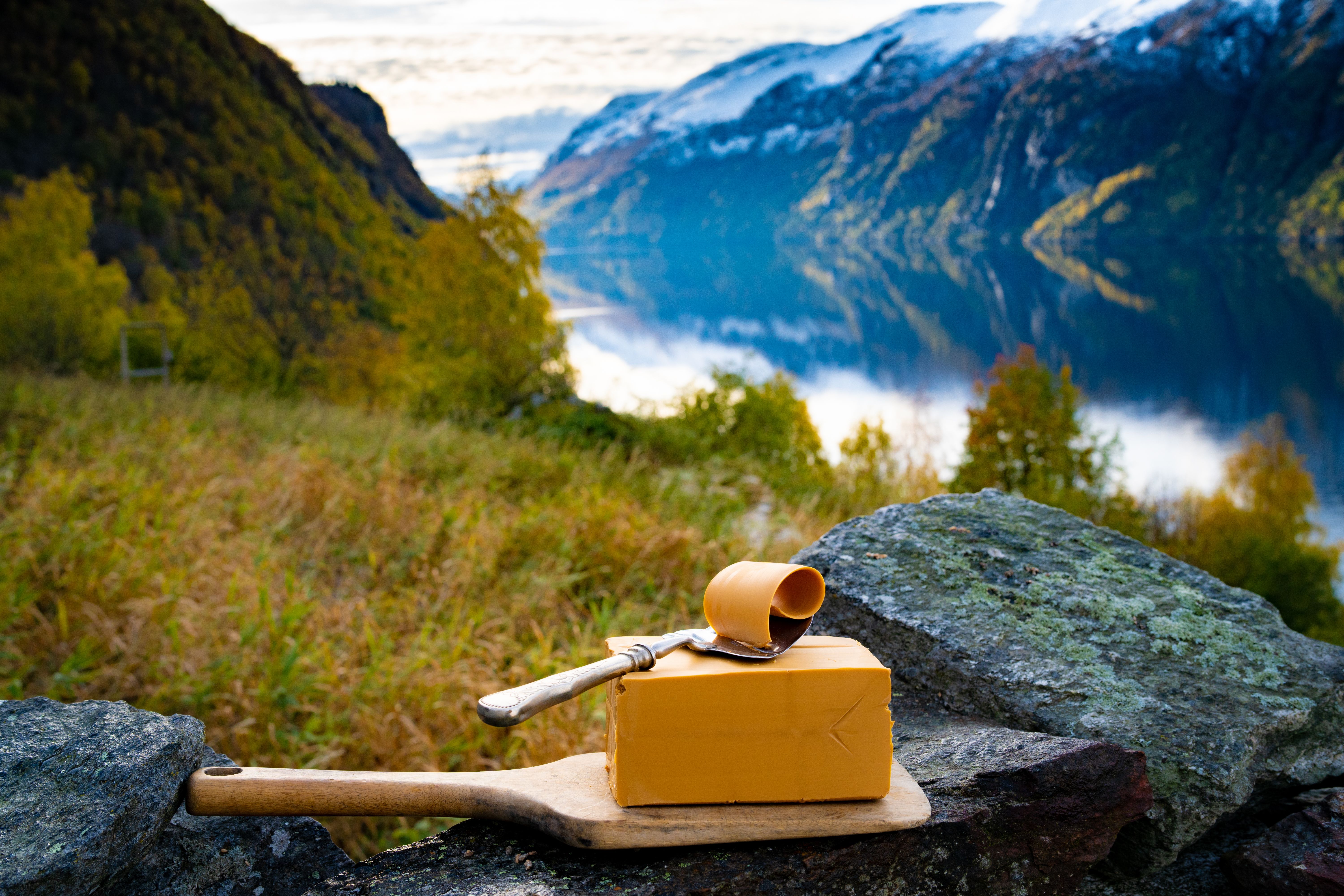 Norwegian brown cheese against a backdrop of mountains and a fjord