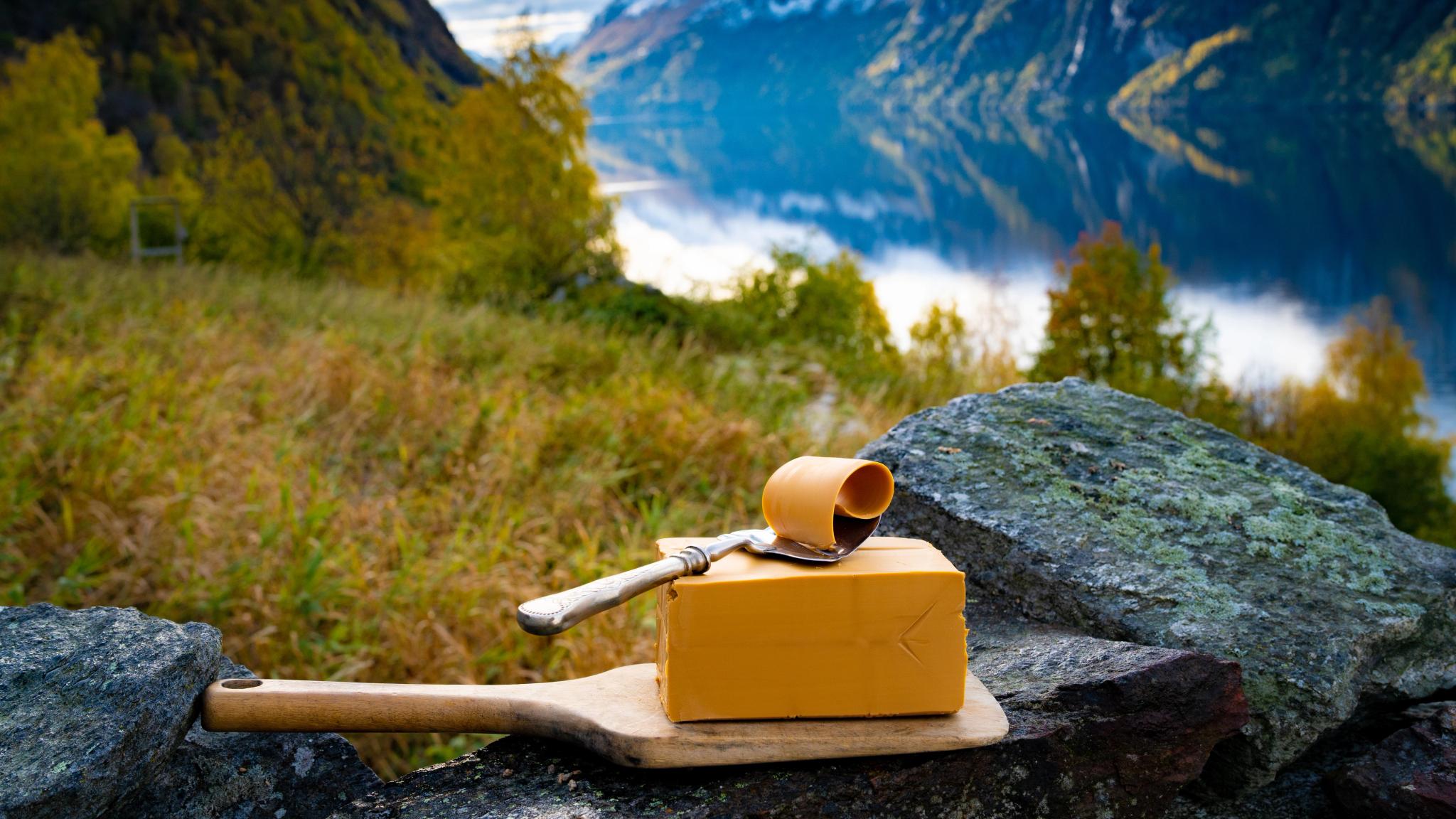 Norwegian brown cheese against a backdrop of mountains and a fjord