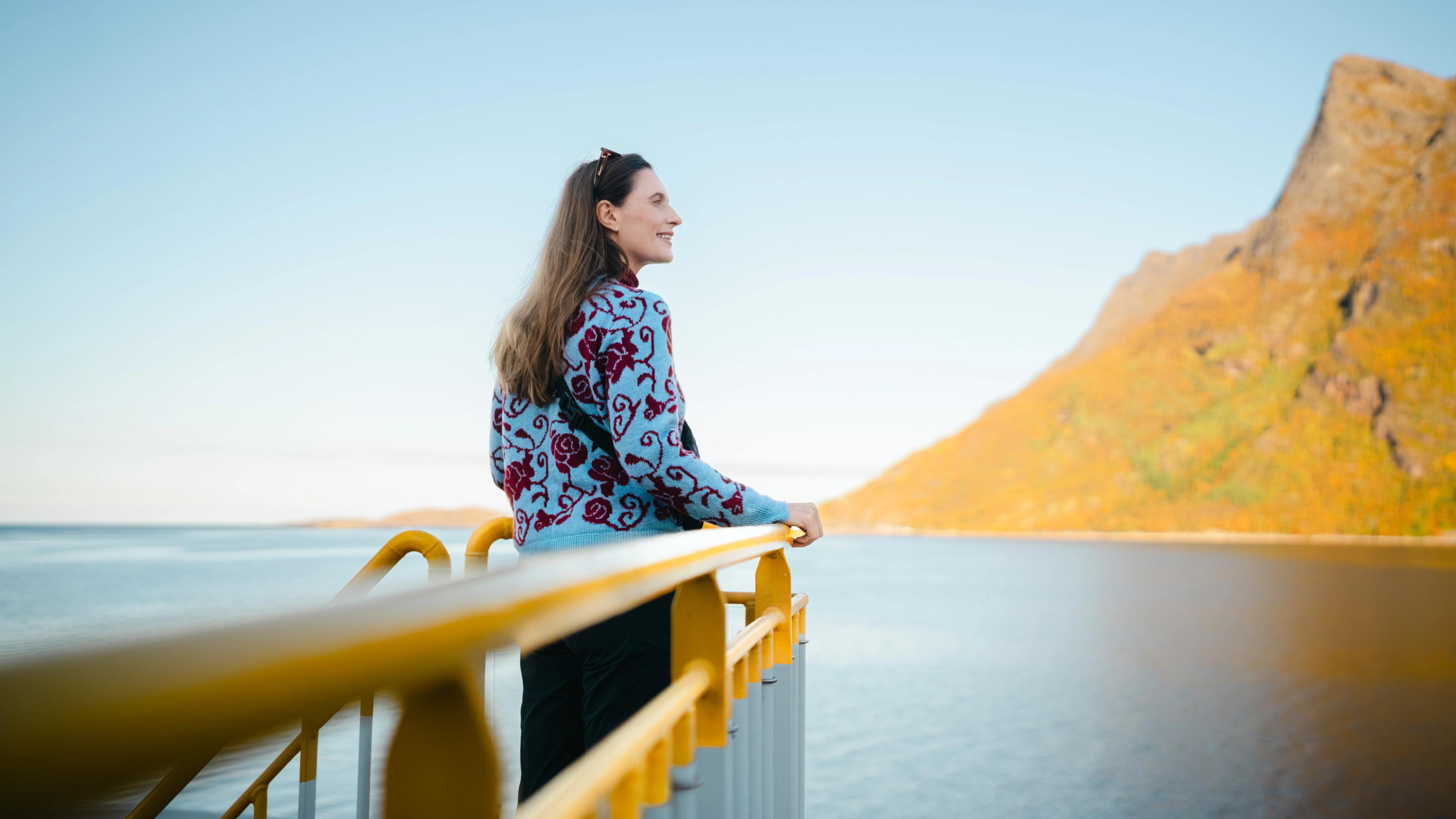 A woman standing on a ferry looking at Kjerringøy, outside og Bodø in Northern Norway.