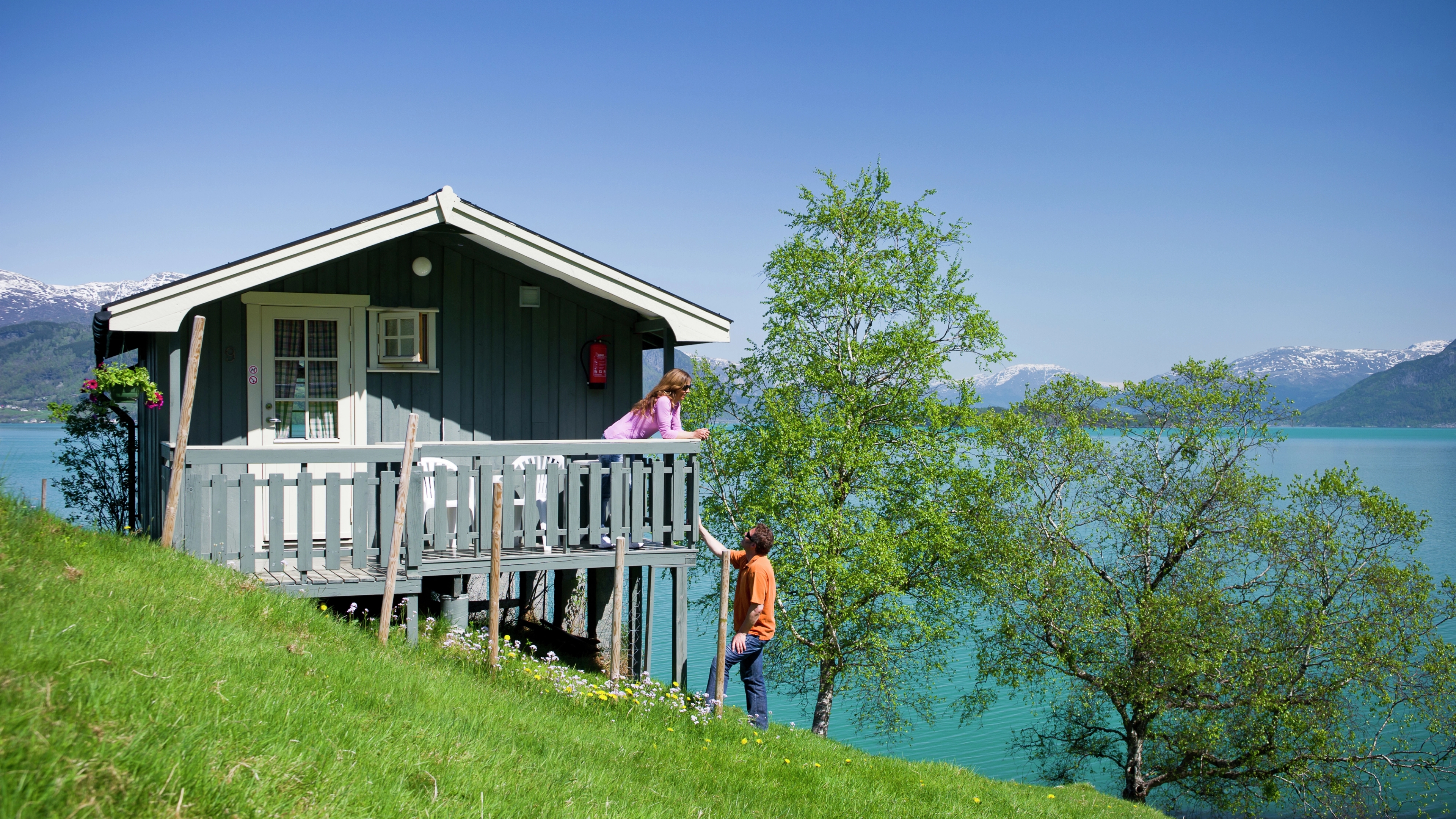 Two people outside of a cabin by the fjord.