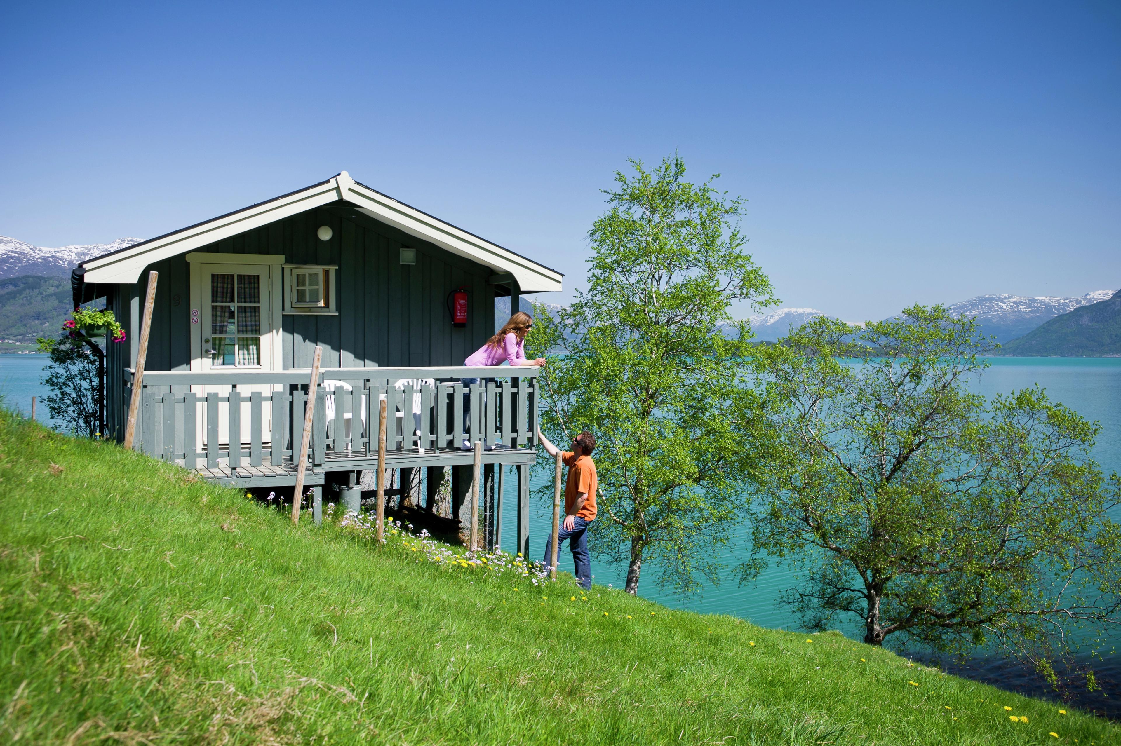 Two people outside of a cabin by the fjord.