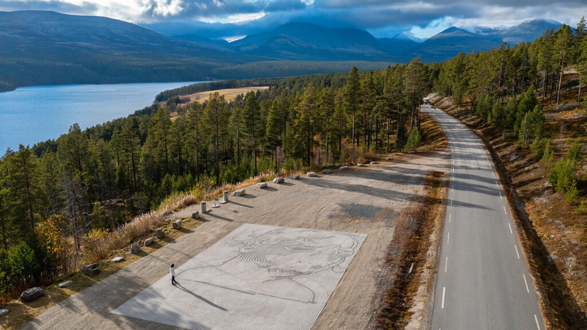 A woman admire art work on the ground in the middle of a vast nature landscape