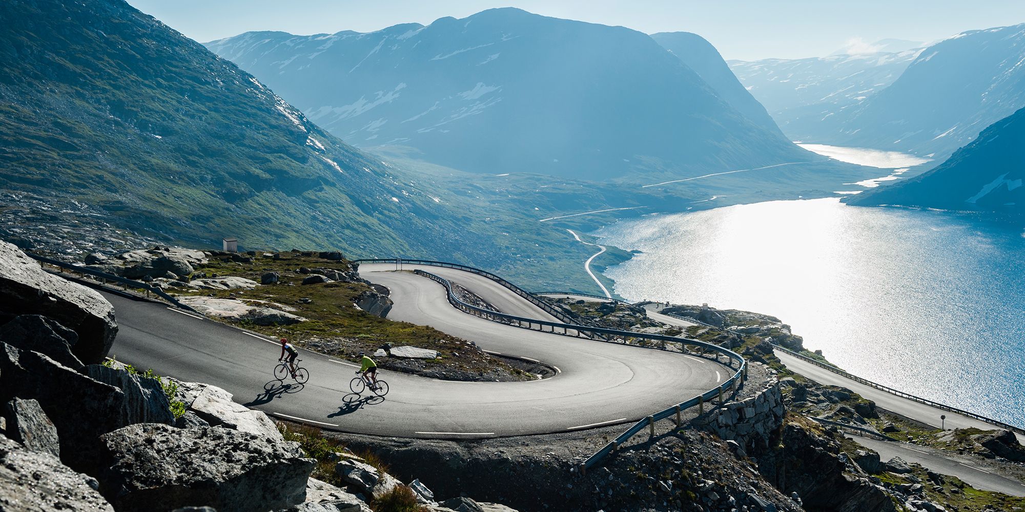 Två personer cyklar längs en slingrande väg ovanför Geirangerfjorden i regionen Fjord Norge (Vestlandet)