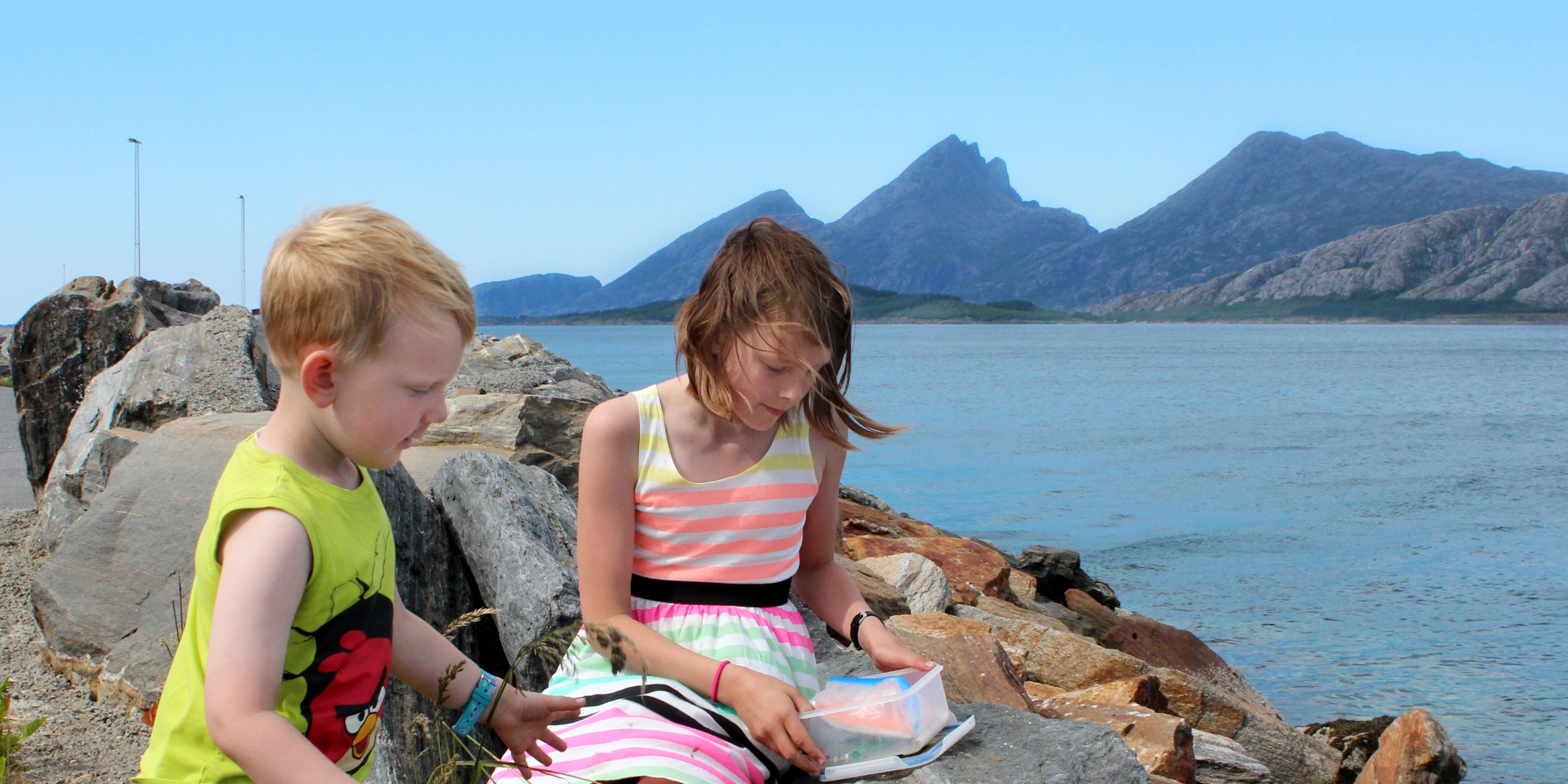 Two kids sitting on rocks next to the sea and try geocaching in Sandnessjøen in Nordland, Northern Norway