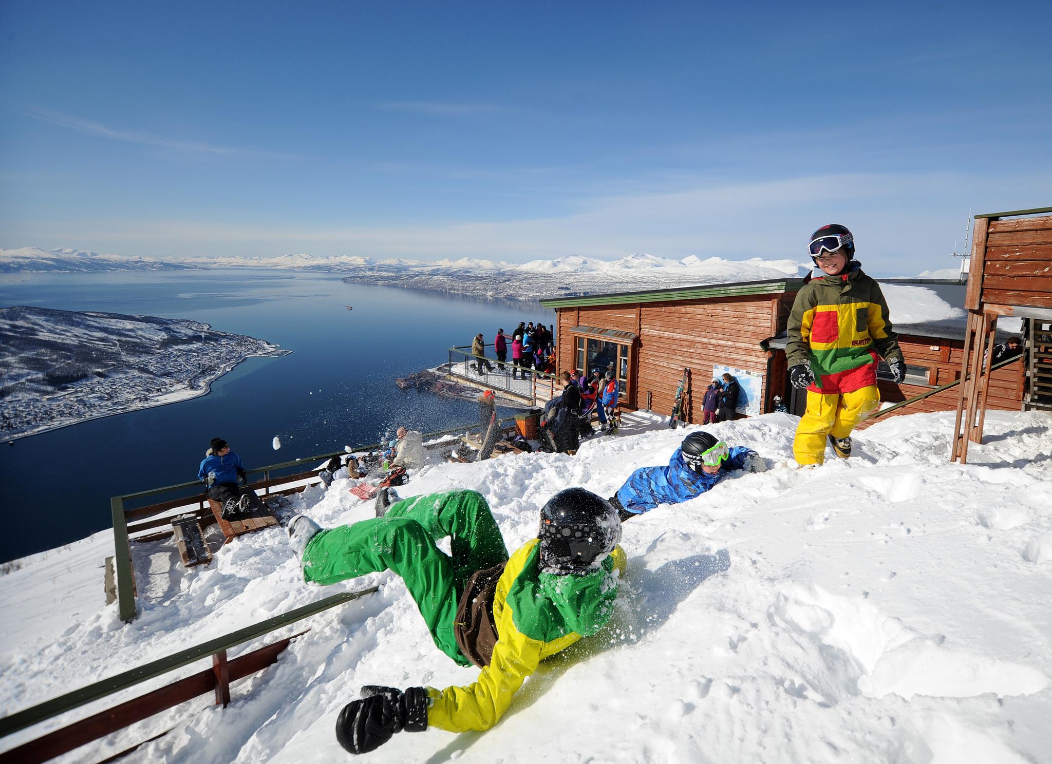 A group of kids playing in the snow at Narvikfjellet ski resort with a wide view of the sea below in Narvik, Northern Norway