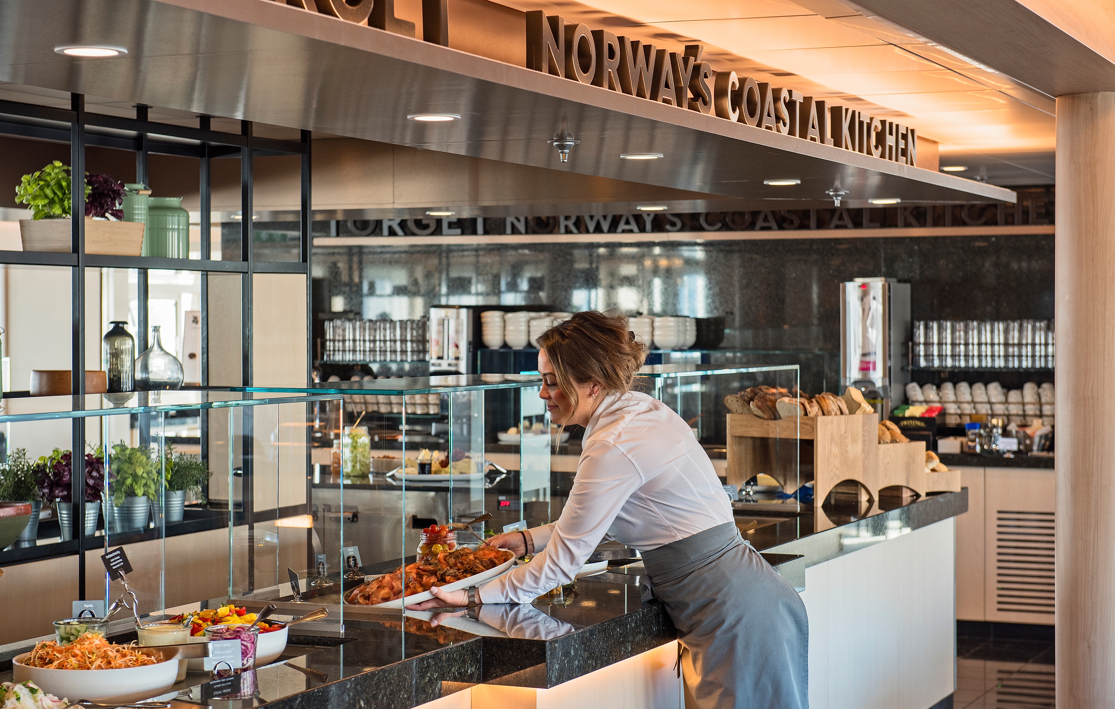 A woman placing food on a buffet table on a Hurtigruten ship