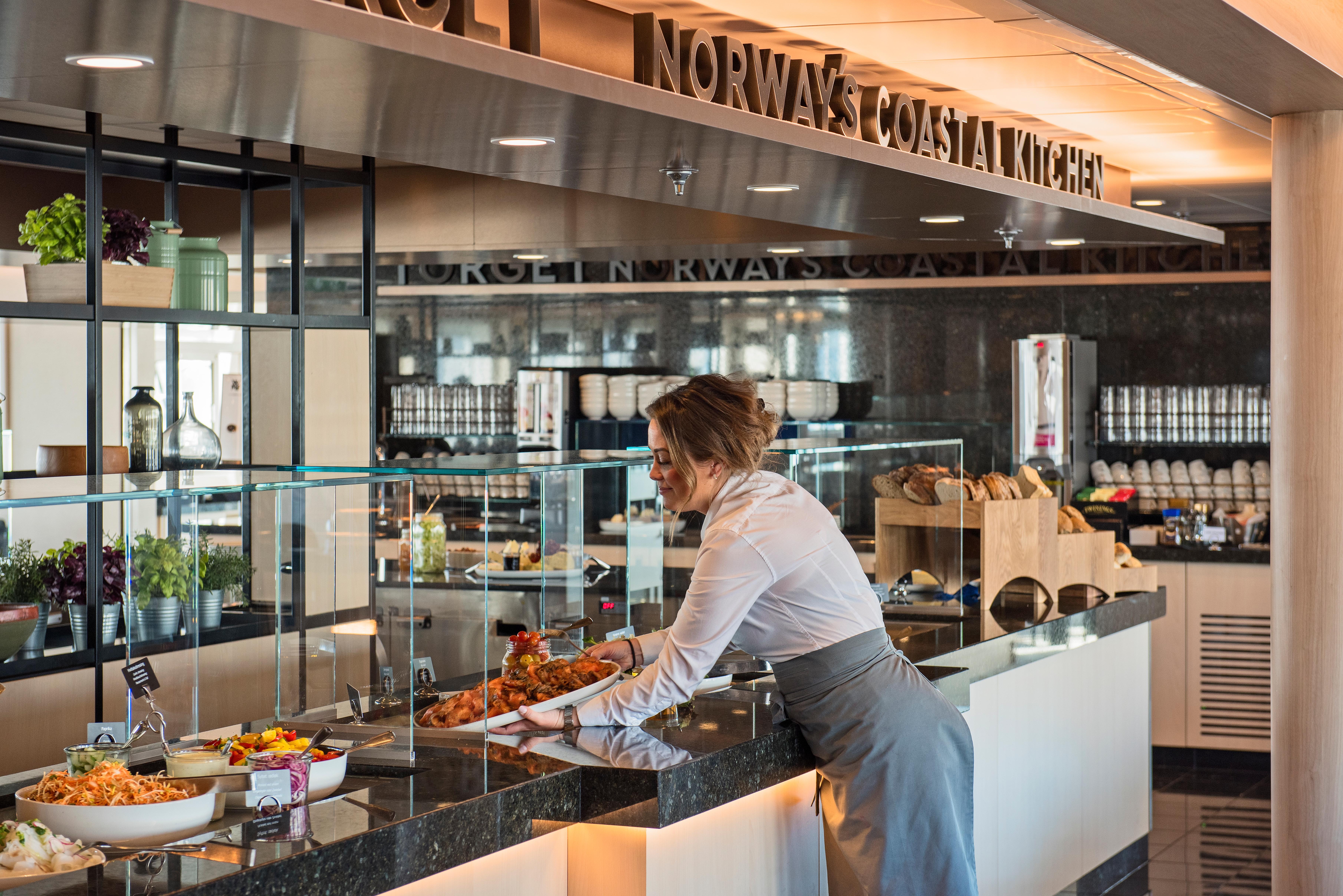 A woman placing food on a buffet table on a Hurtigruten ship