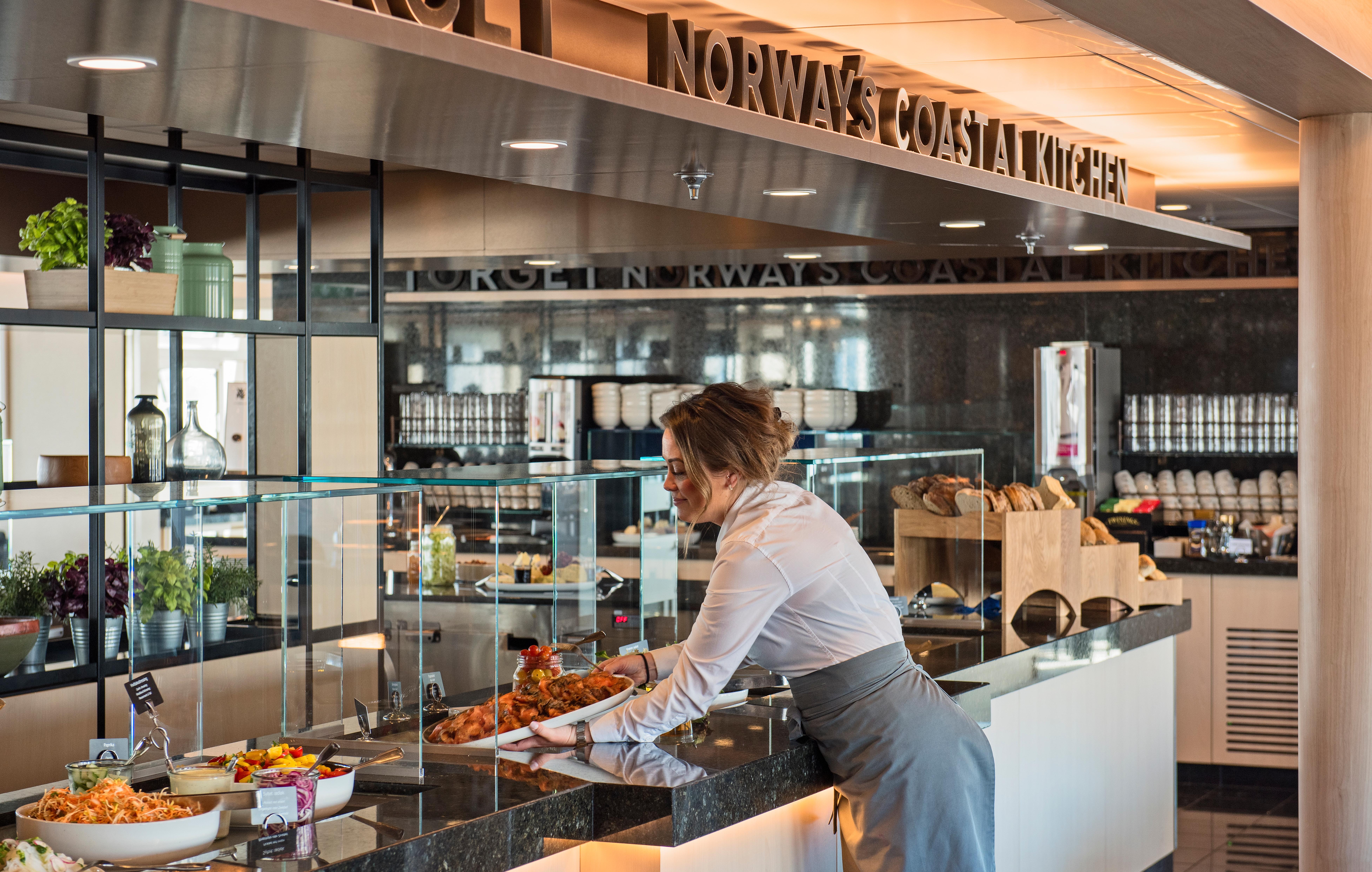 A woman placing food on a buffet table on a Hurtigruten ship