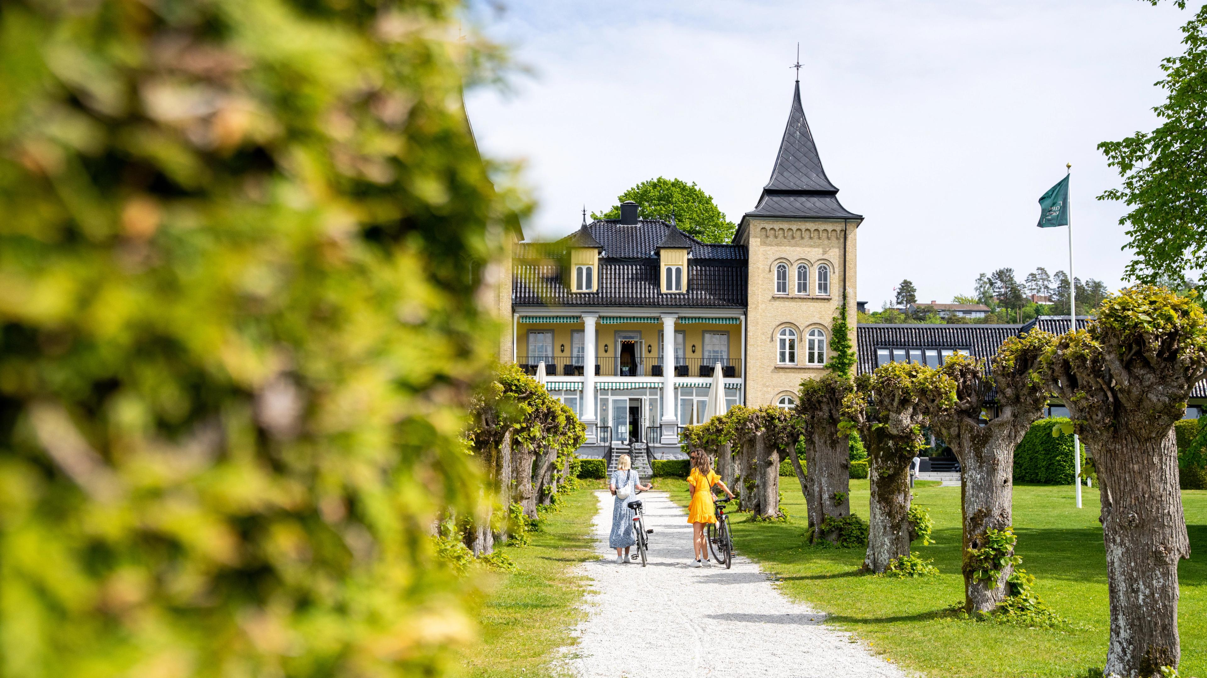 Two women walking with bikes in front of Refsnes Gods at Jeløy in Moss