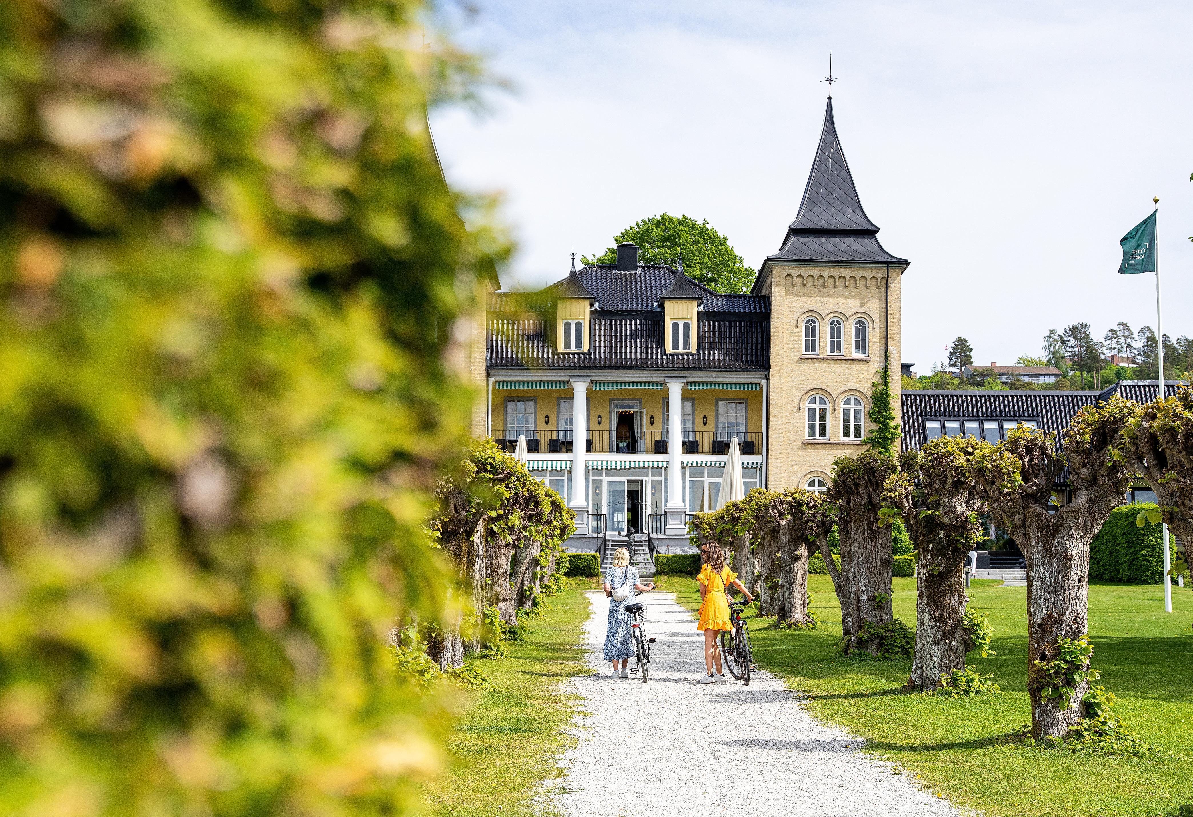 Two women walking with bikes in front of Refsnes Gods at Jeløy in Moss