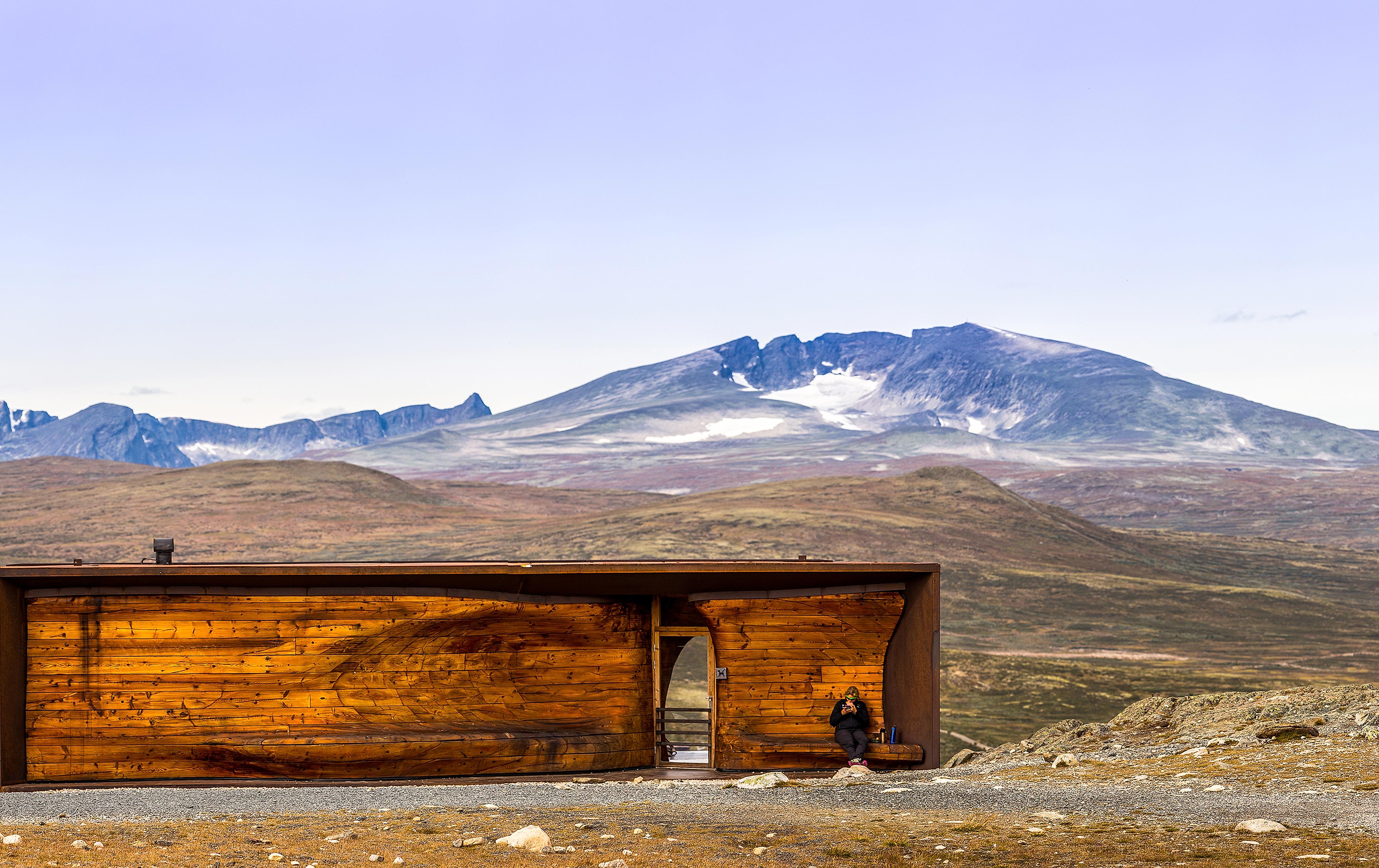 A person at the Viewpoint Snøhetta pavillion with the mountain Snøhetta in the background. Dovrefjell, Eastern Norway.
