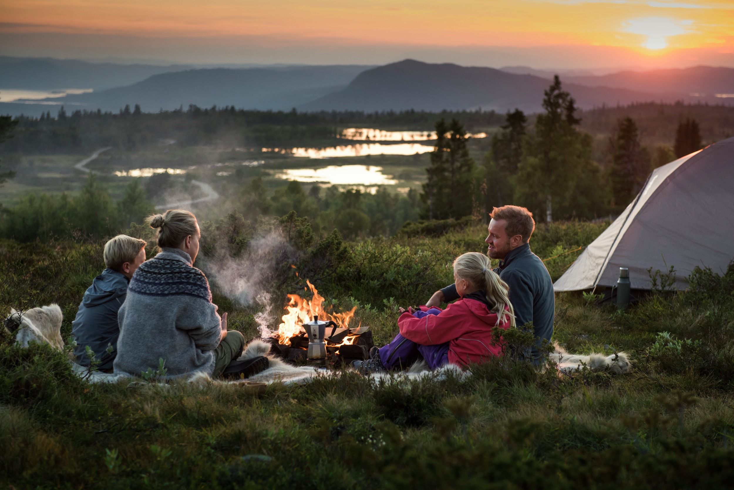 Familie på fire sitter ved et bål ved siden av teltet i Uvdal