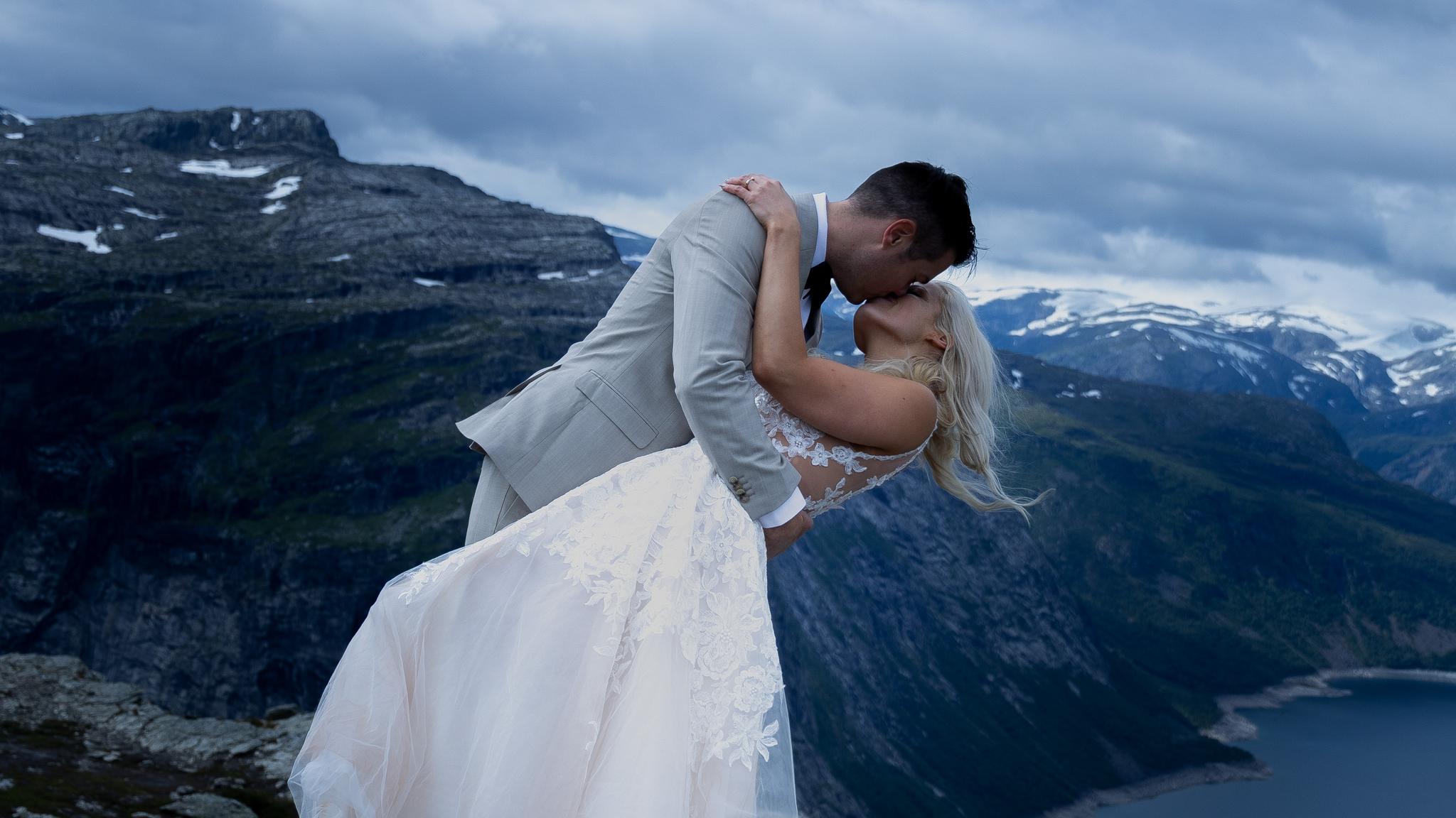 A newly wed couple kissing at the top of Trolltunga in Ullensvang in Fjord Norway